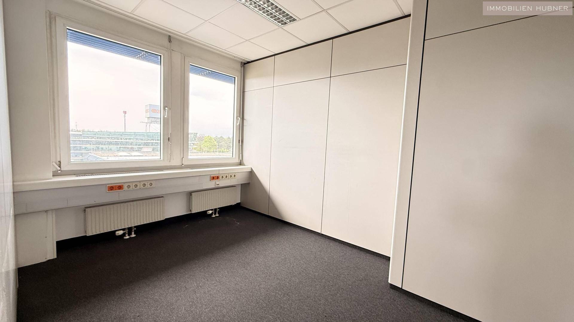 Kleineres Büro mit Teppichboden, zwei Fenstern und praktischen Einbauschränken, ideal für Einzelarbeitsplätze.