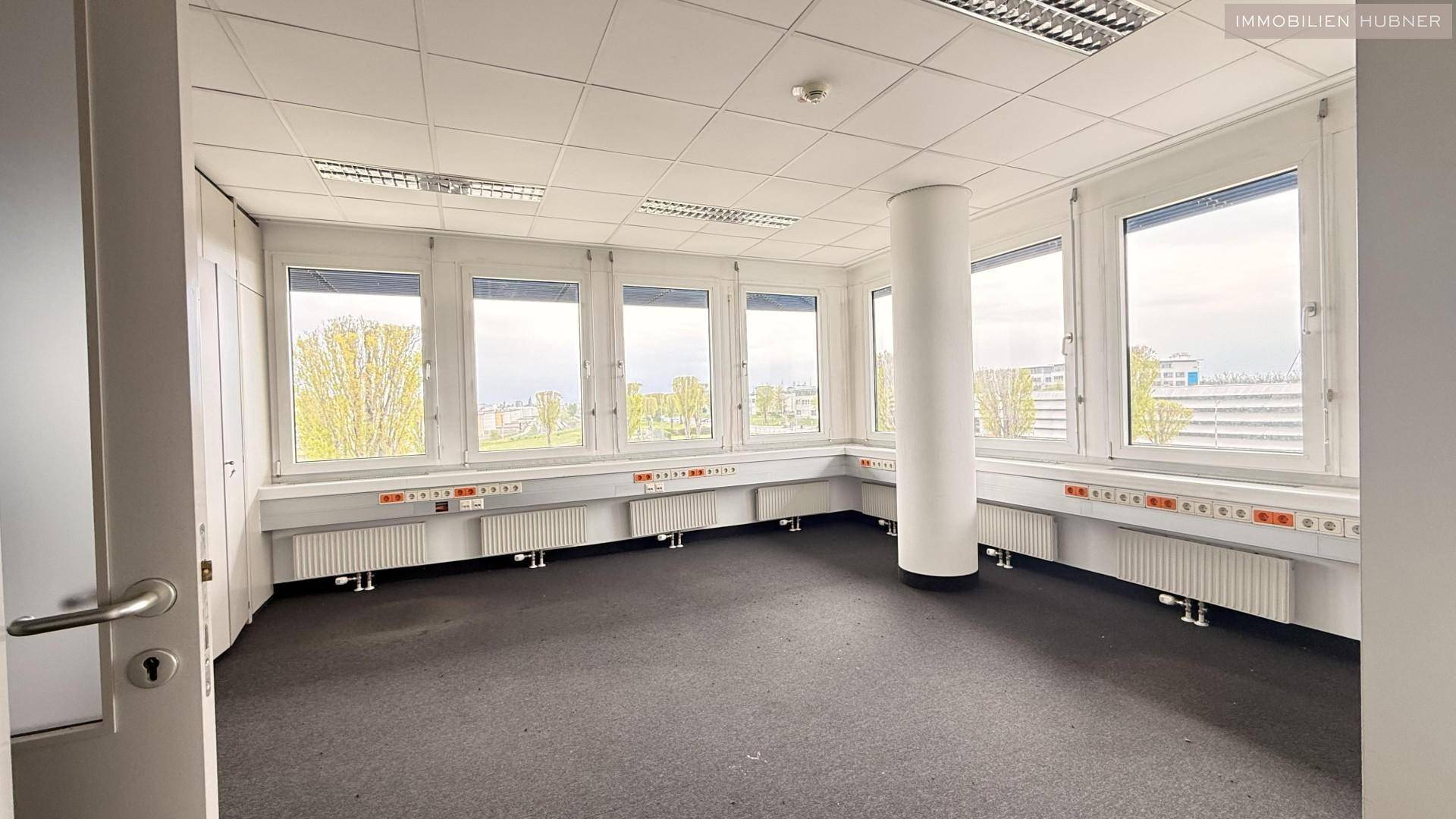 Eckbüro mit vielen Fenstern, Teppichboden und einem zentralen Pfeiler, der den Raum strukturiert.