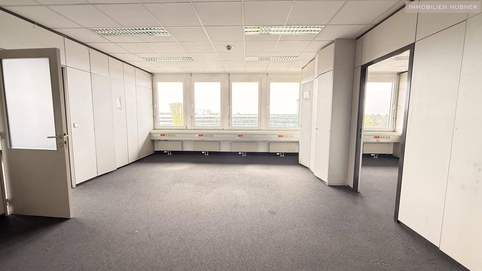 Helles Büro mit Teppichboden, integrierten Wandschränken und großen Fenstern für eine angenehme Arbeitsatmosphäre.