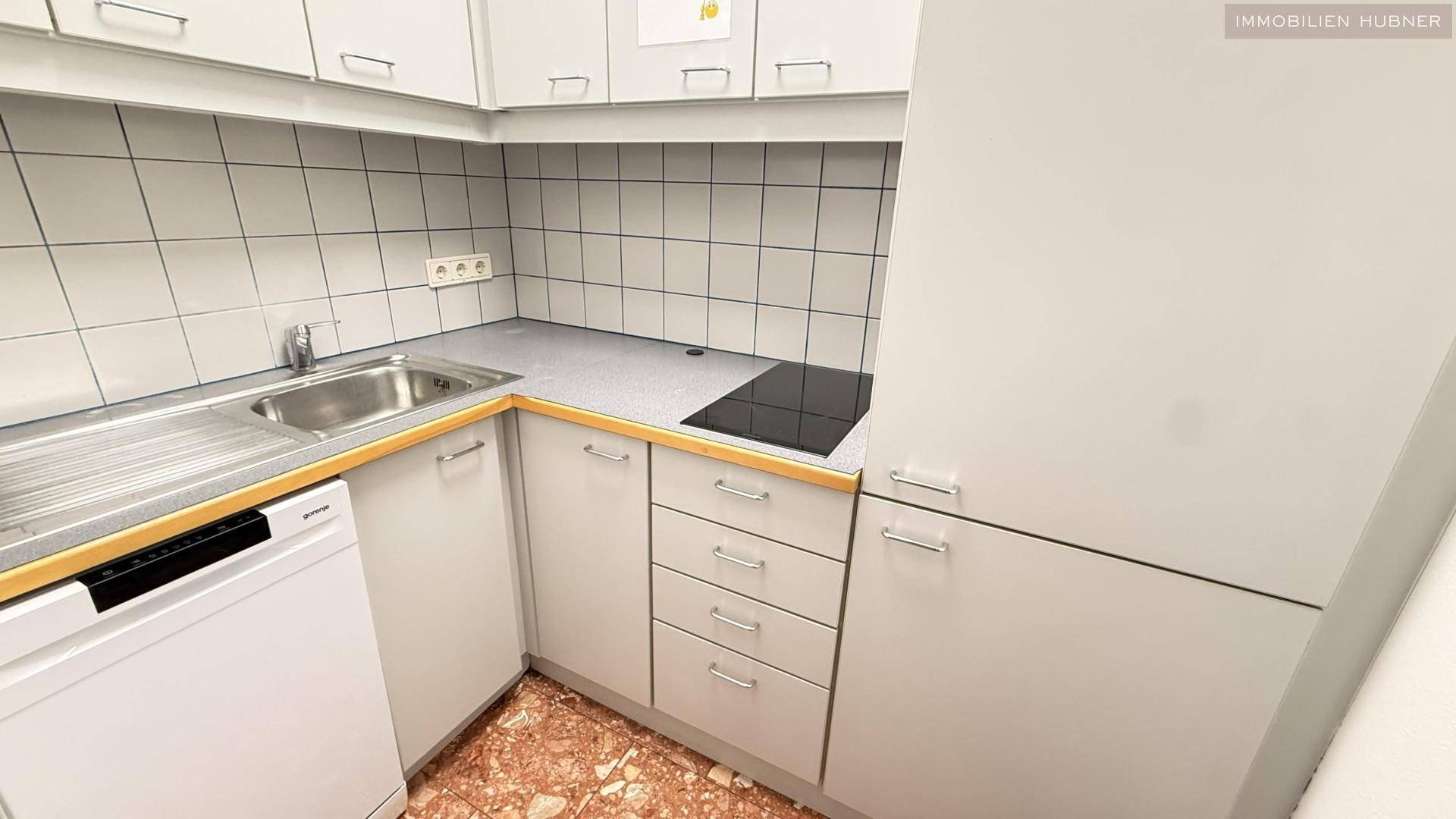 Kleine Küchenzeile mit weißen Schränken, Fliesenrückwand, Spüle und Induktionskochfeld, ideal für Pausen.