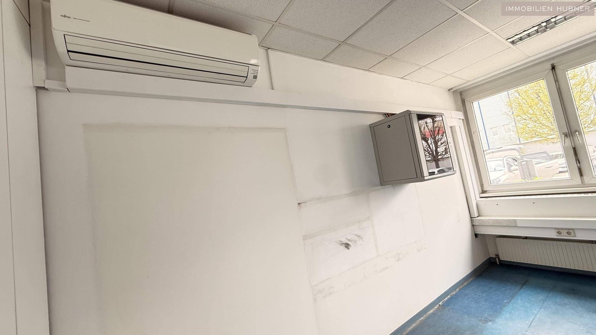 Detailansicht eines Bürobereichs mit Klimaanlage und einem Fenster, das Tageslicht spendet.