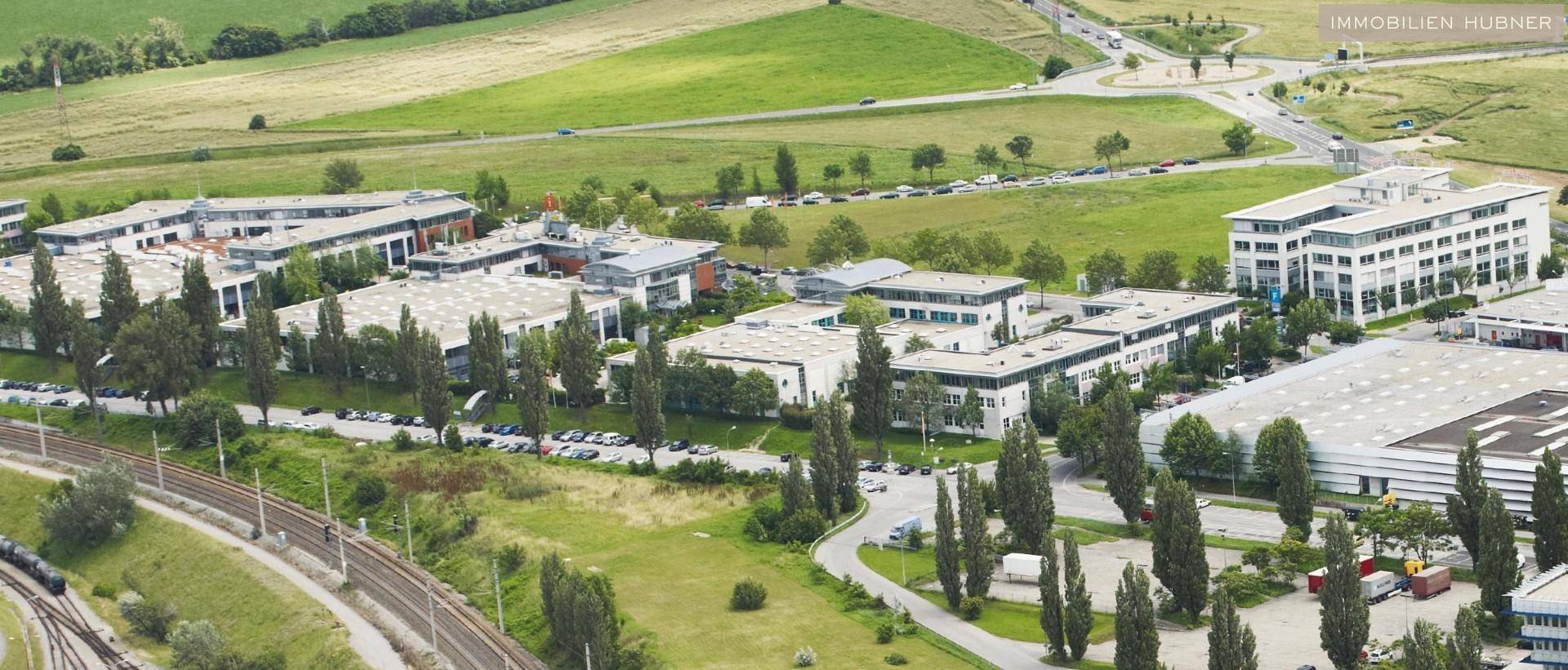Weitläufige Luftaufnahme eines Gewerbegebiets mit Bürobauten, viel Grün und einer gut ausgebauten Infrastruktur.