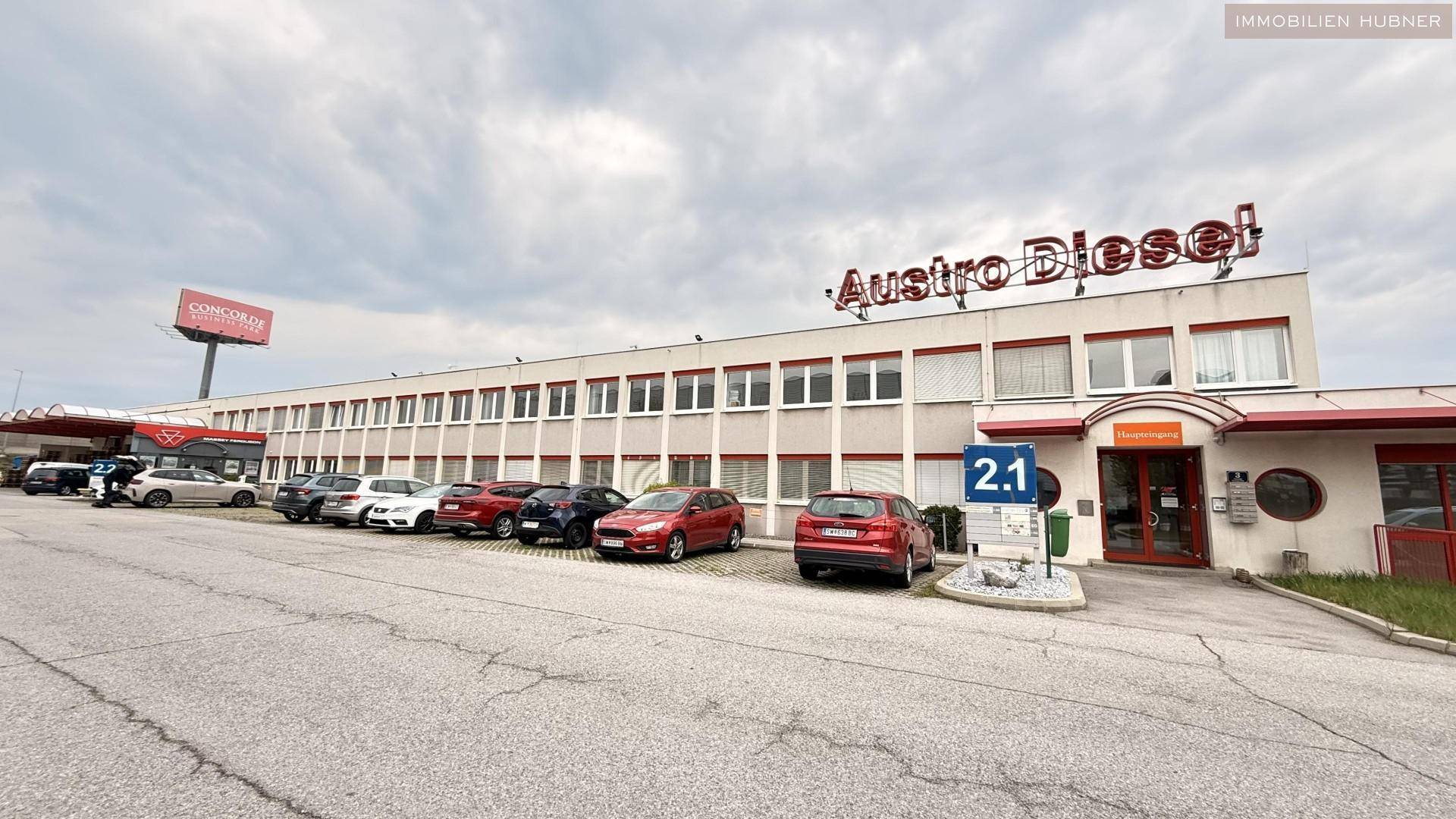Außenansicht eines Geschäftsgebäudes mit Parkplätzen davor und einem großen Schriftzug an der Fassade.