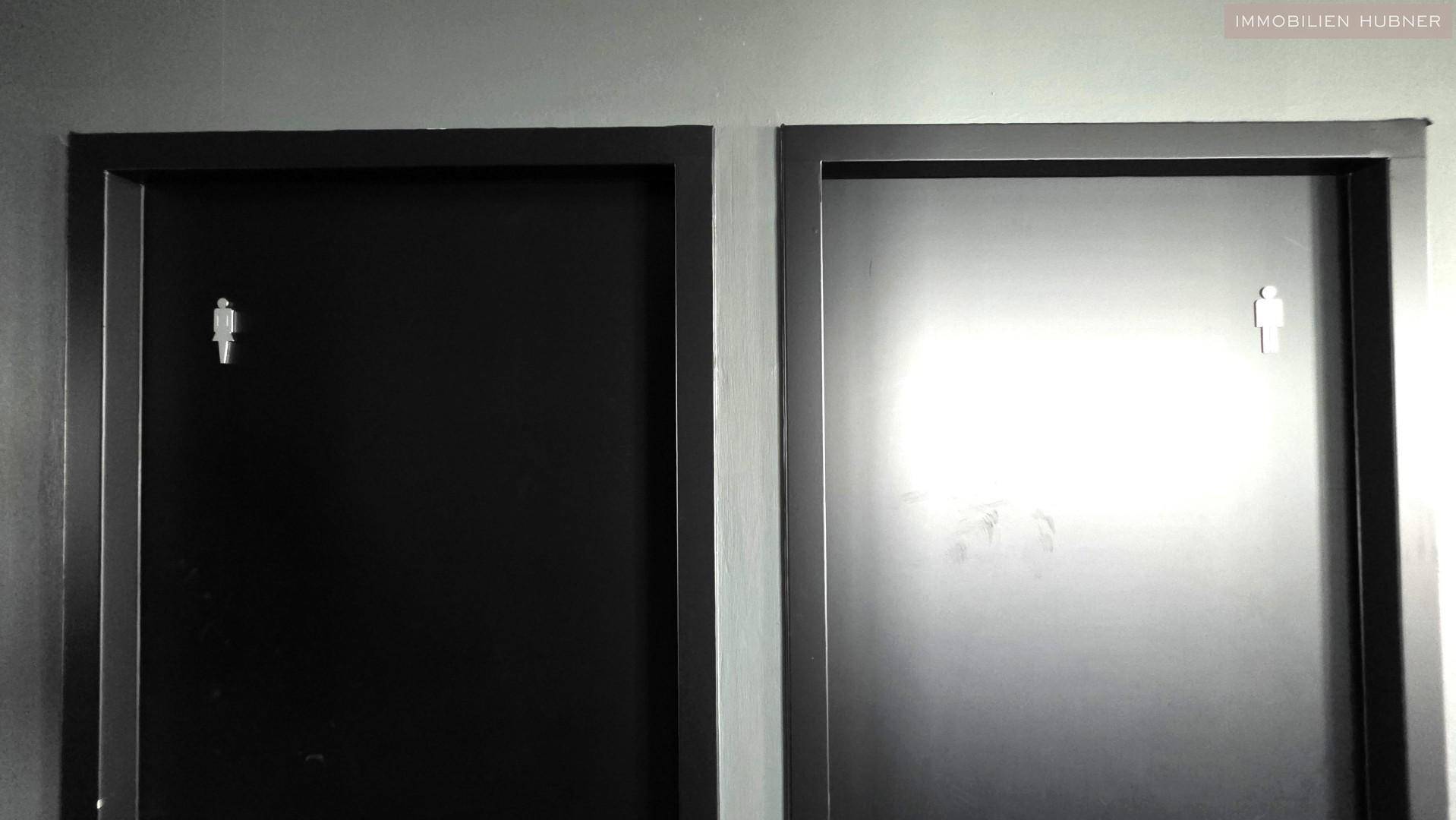 Zwei schwarze Türen zu den Toilettenbereichen mit deutlichen Piktogrammen.