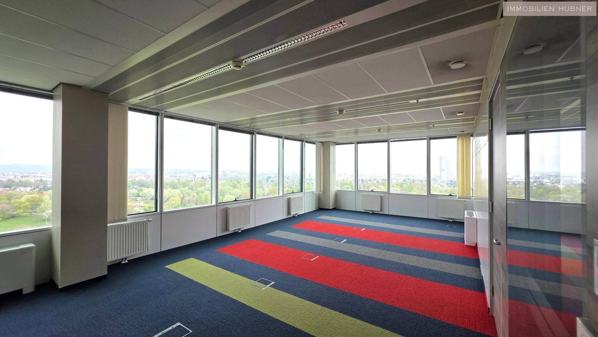Helles Büro mit farbenfrohem Teppichboden und weitem Blick auf die grüne Umgebung.