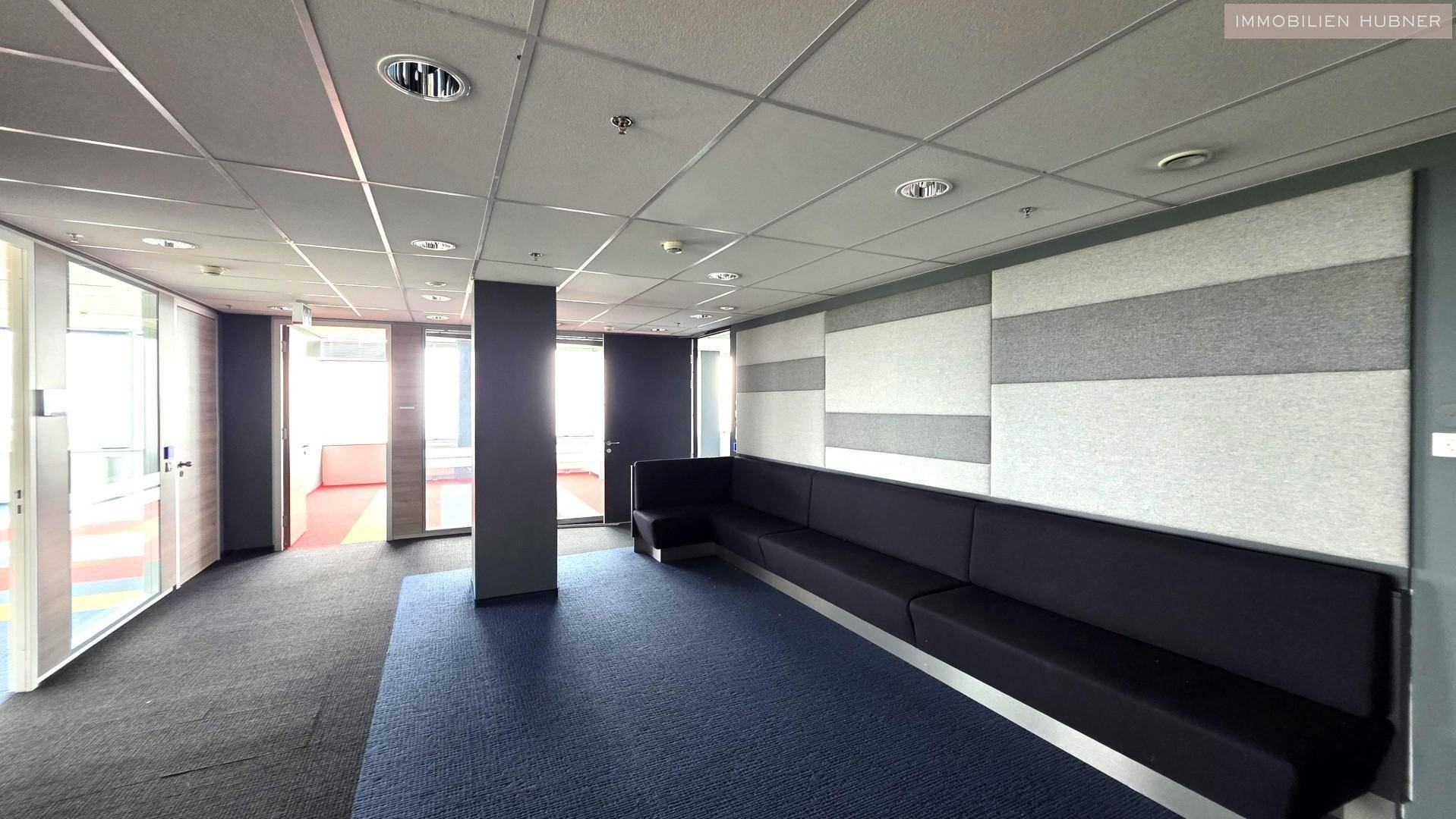 Moderner Loungebereich mit langer Sitzbank, Teppichboden und schallabsorbierenden Wandpaneelen.