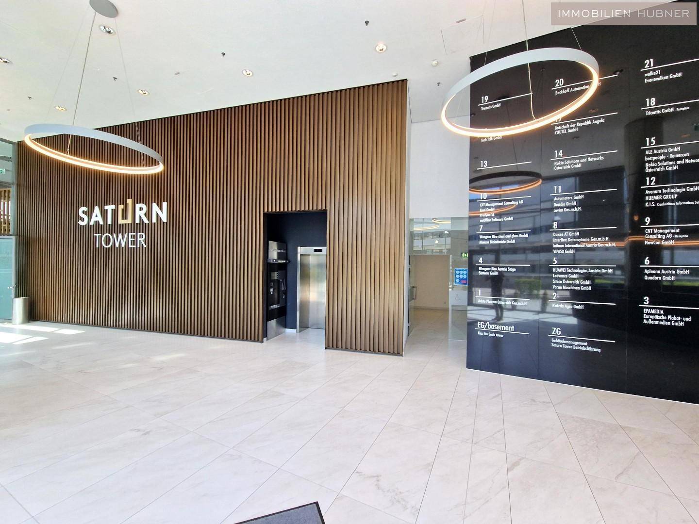 Geräumige Lobby mit Holzwandverkleidung, Aufzügen und digitalen Informationsanzeigen.