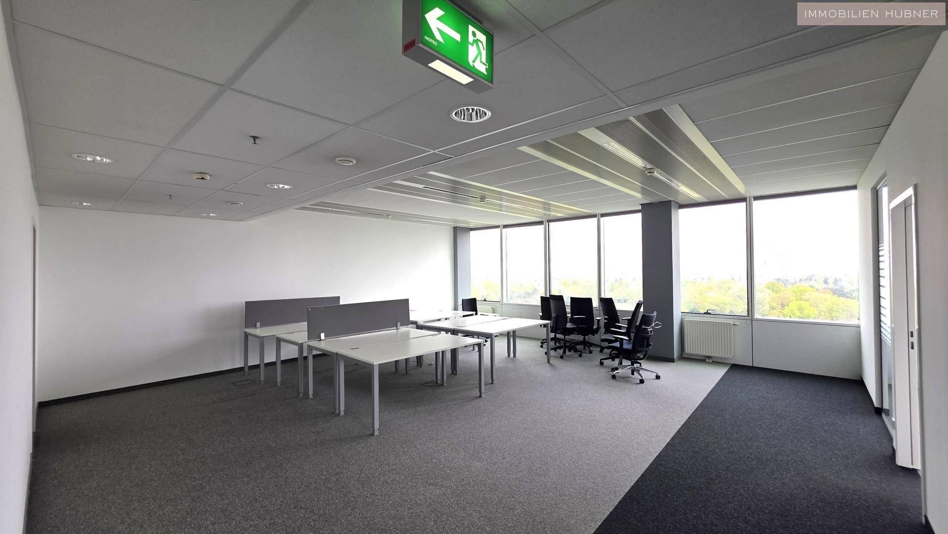 Modern eingerichtetes Büro mit mehreren Arbeitsplätzen und Blick ins Grüne durch große Fenster.