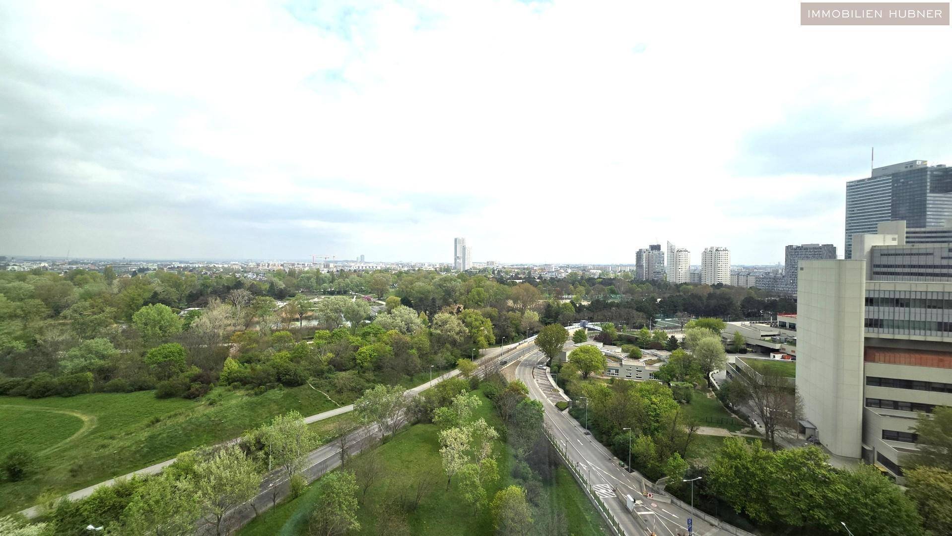 Weitläufiger Blick aus dem Fenster über grüne Parkanlagen und die Skyline der Stadt.