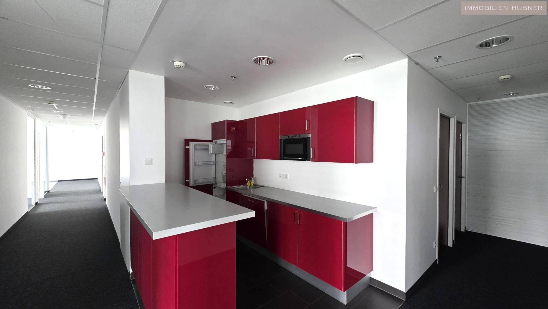 Moderne Teeküche mit roten Hochglanzschränken, integrierter Mikrowelle und Kühlschrank.