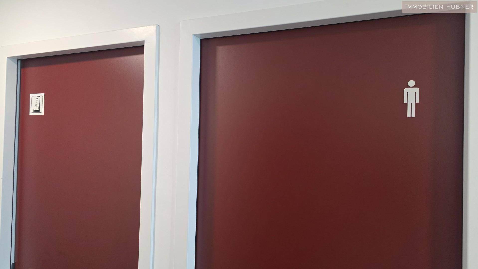 Zwei rote Türen zu den Toilettenbereichen, eine davon mit einem Männchen-Symbol gekennzeichnet.