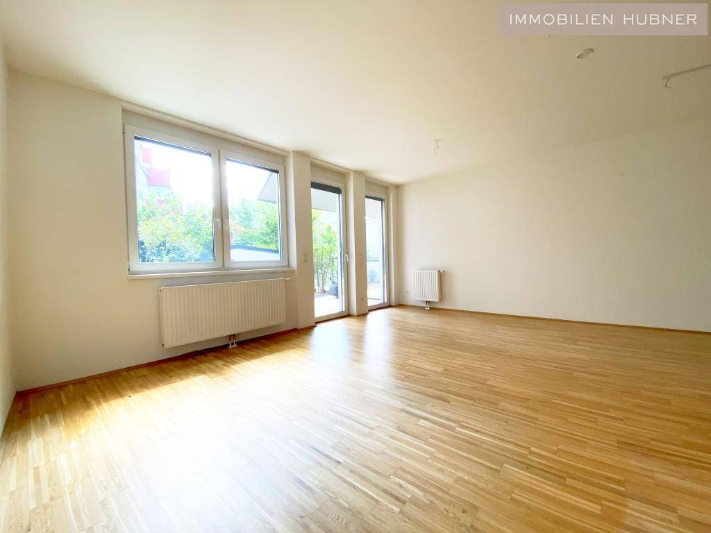 Helles, leeres Zimmer mit Parkettboden und großen Fenstern sowie Zugang zur Terrasse.