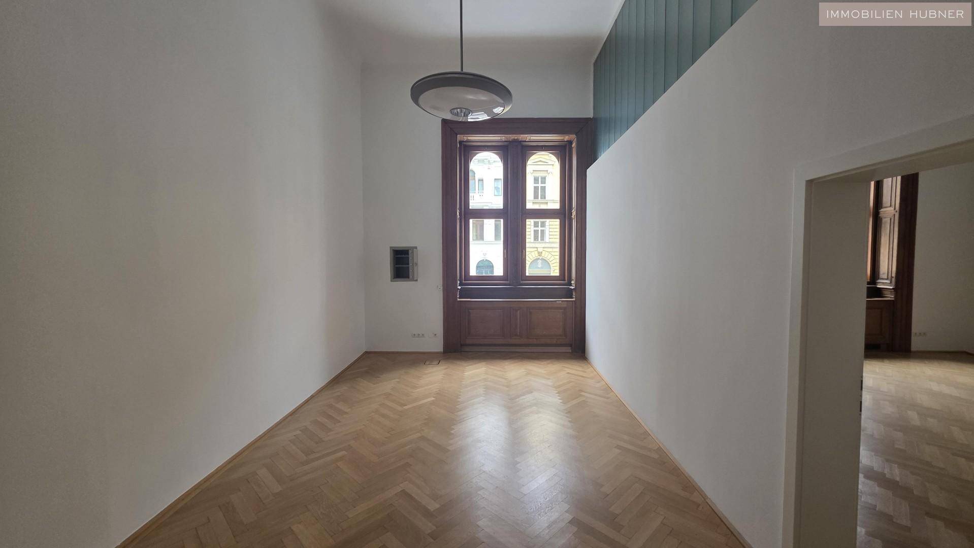 Heller Wohnraum mit hohen Decken, großen Fenstern und klassischem Fischgrätparkettboden.