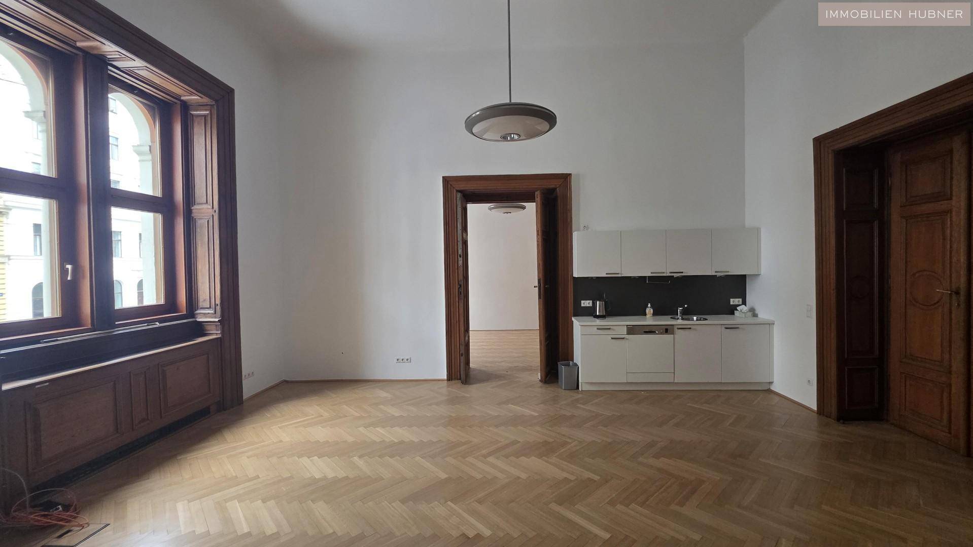 Offener Wohnbereich mit integrierter Küchenzeile, Holztüren und elegantem Fischgrätparkett.
