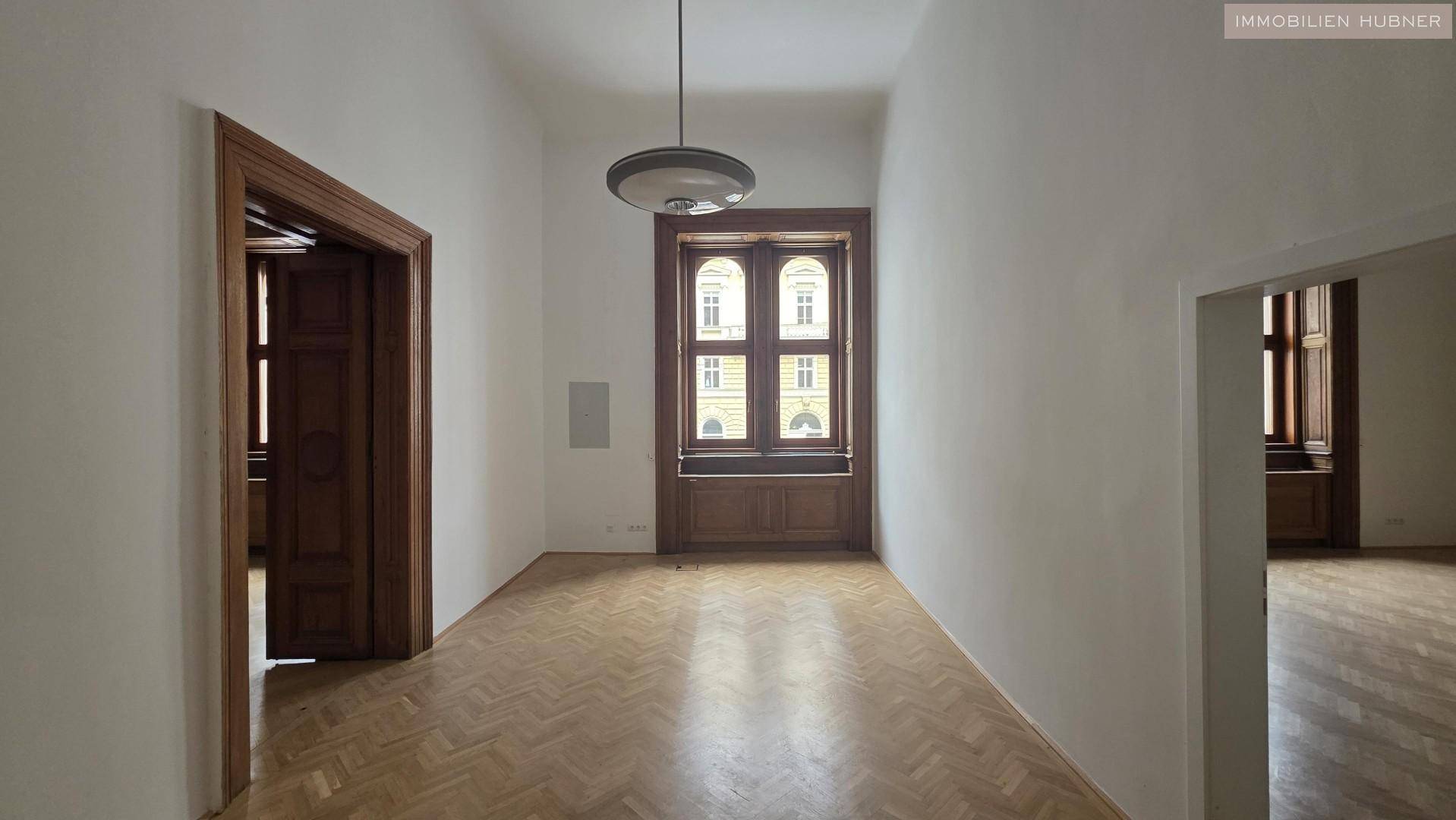 Heller Flur mit hohen Decken, großen Fenstern und klassischem Fischgrätparkettboden.