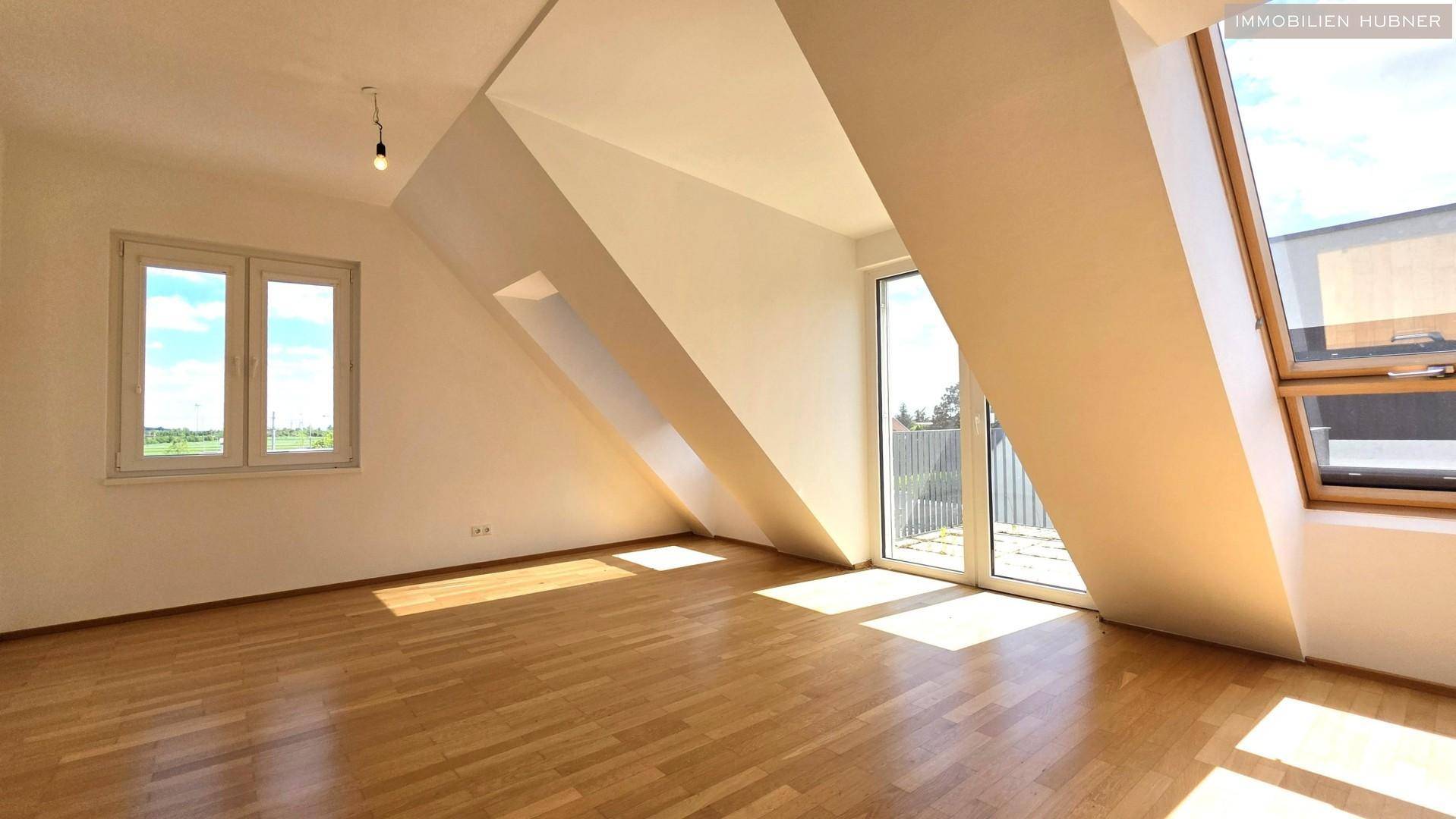 Lichtdurchfluteter Raum mit Parkettboden und großen Fenstern, die viel Tageslicht hereinlassen.