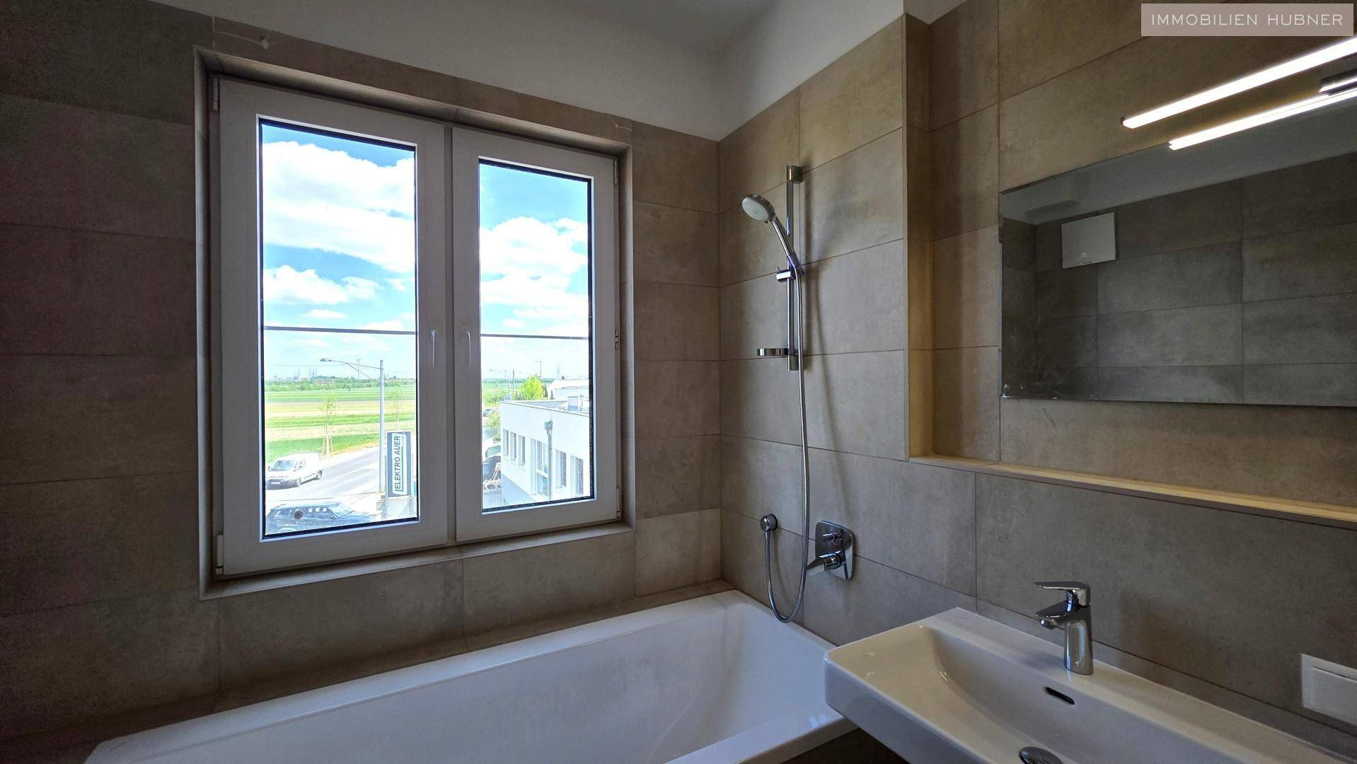 Detailansicht des Badezimmers mit Badewanne, Duscharmatur und Fenster mit Ausblick.