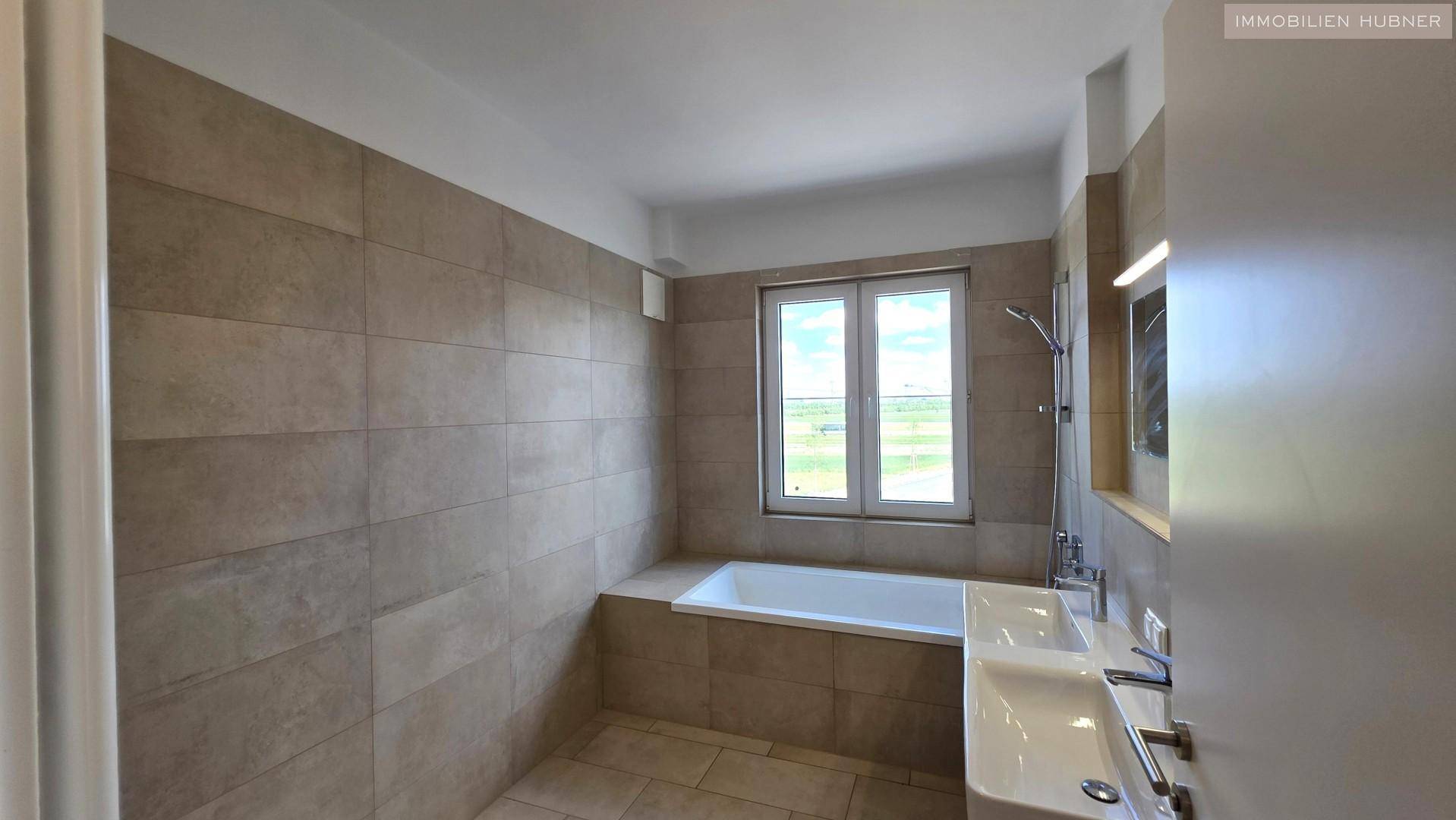 Modernes Badezimmer mit beigefarbenen Fliesen, Badewanne und Doppelwaschbecken.