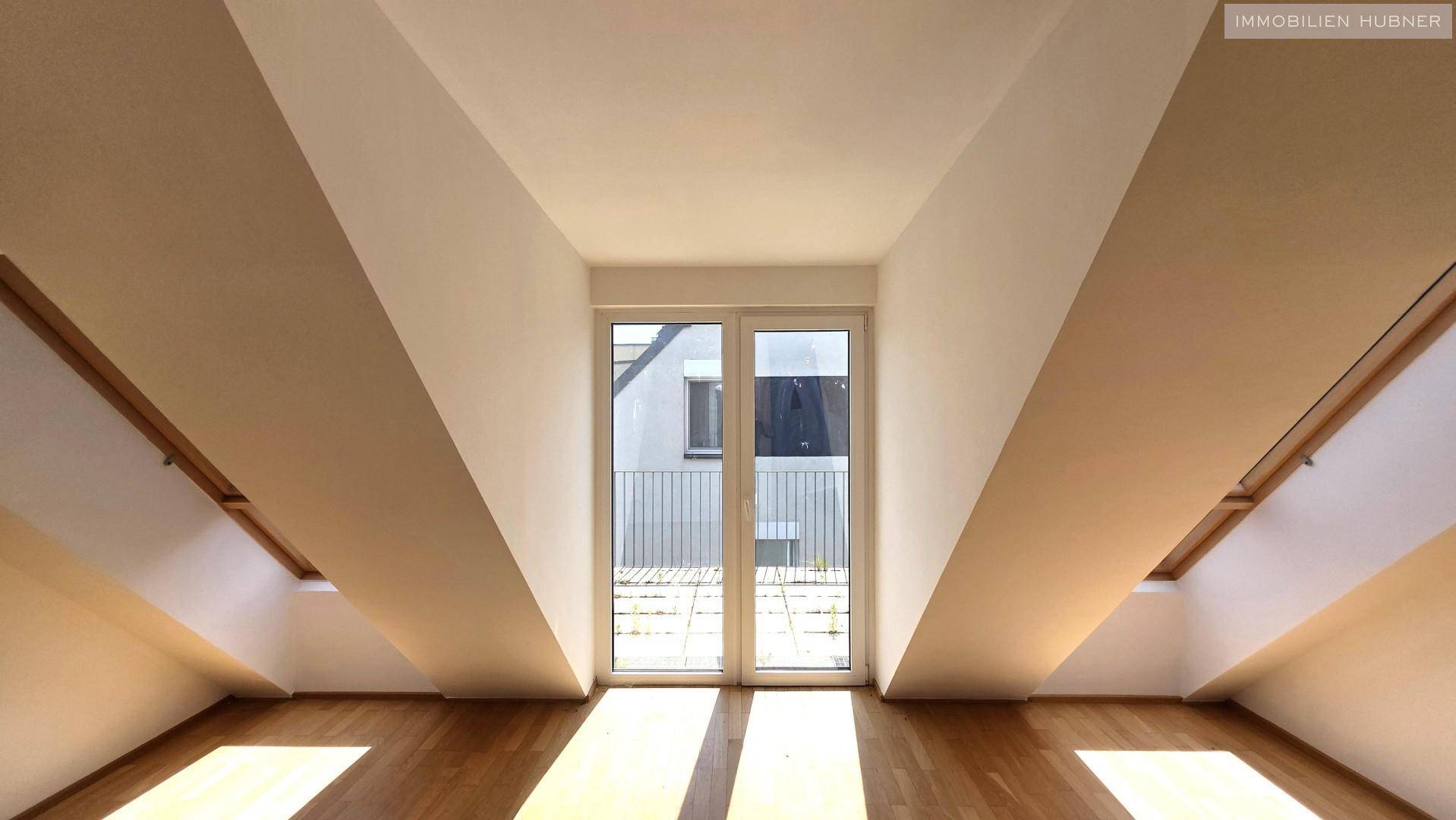 Heller Raum mit Holzboden und Balkontür, die den Blick nach draußen freigibt.