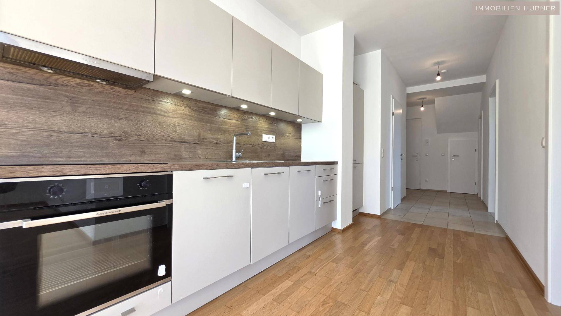 Moderne Einbauküche mit grauen Schränken, Holzakzenten und integriertem Backofen.