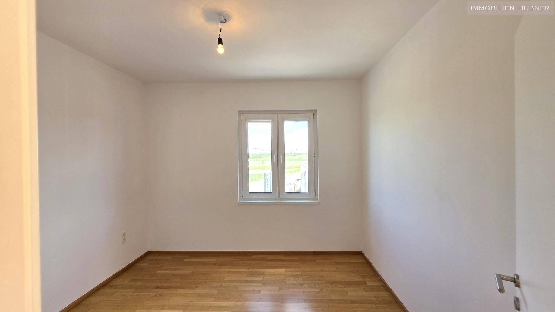 Helles Schlafzimmer mit Parkettboden und großem Fenster, das viel Licht spendet.