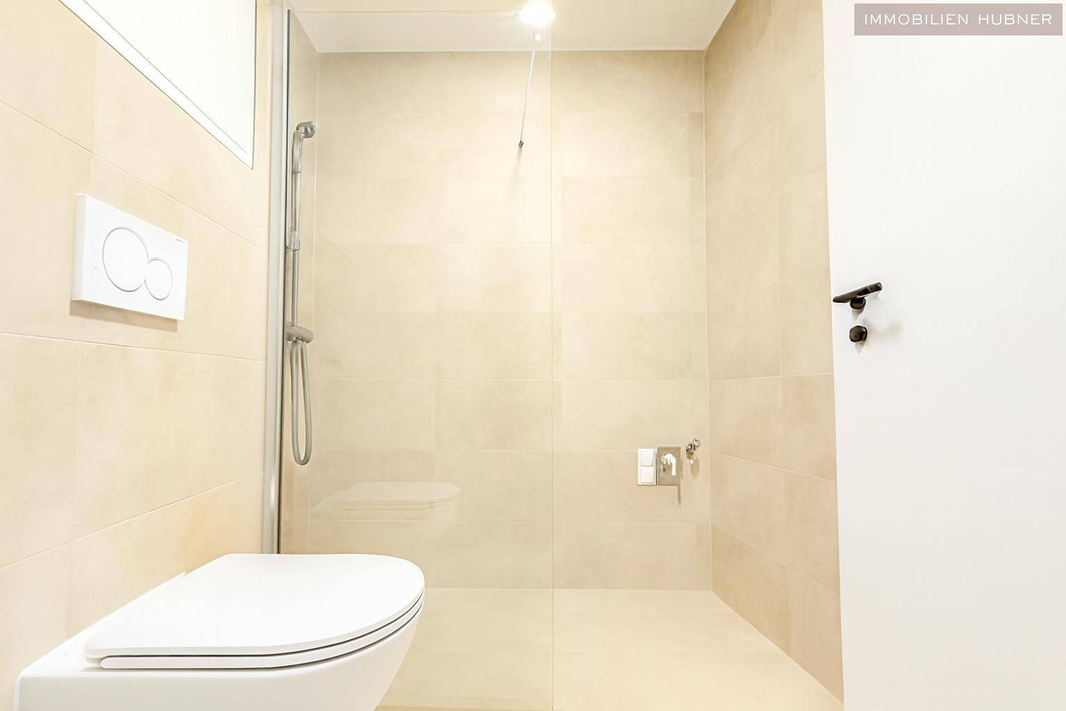 Zeitgemäßes Badezimmer mit beigefarbenen Fliesen, Duschbereich und wandhängendem WC, hell und funktional.