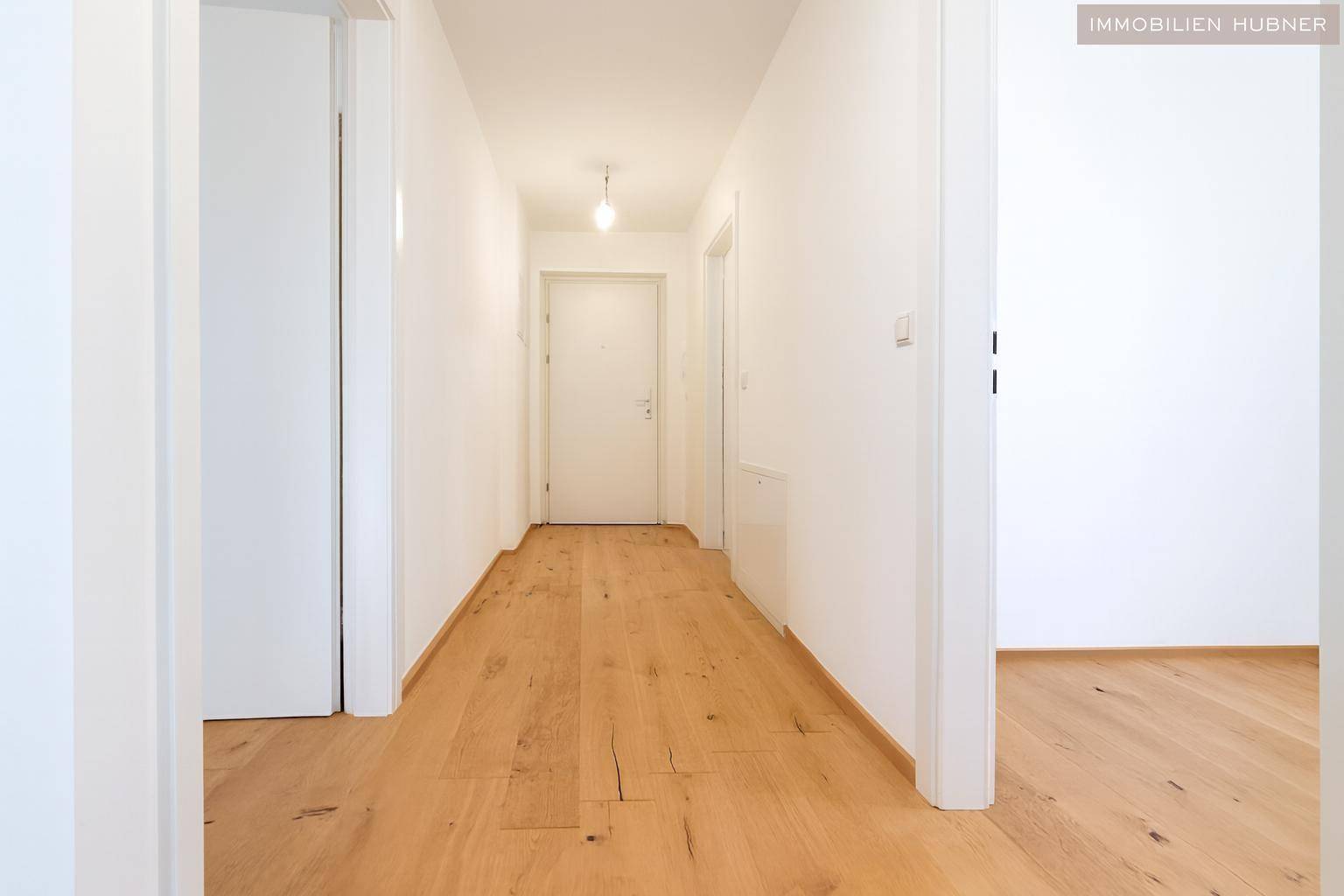 Geräumiger Flur mit Holzboden und weiß gestrichenen Wänden, der zu den Zimmern führt, sehr hell.
