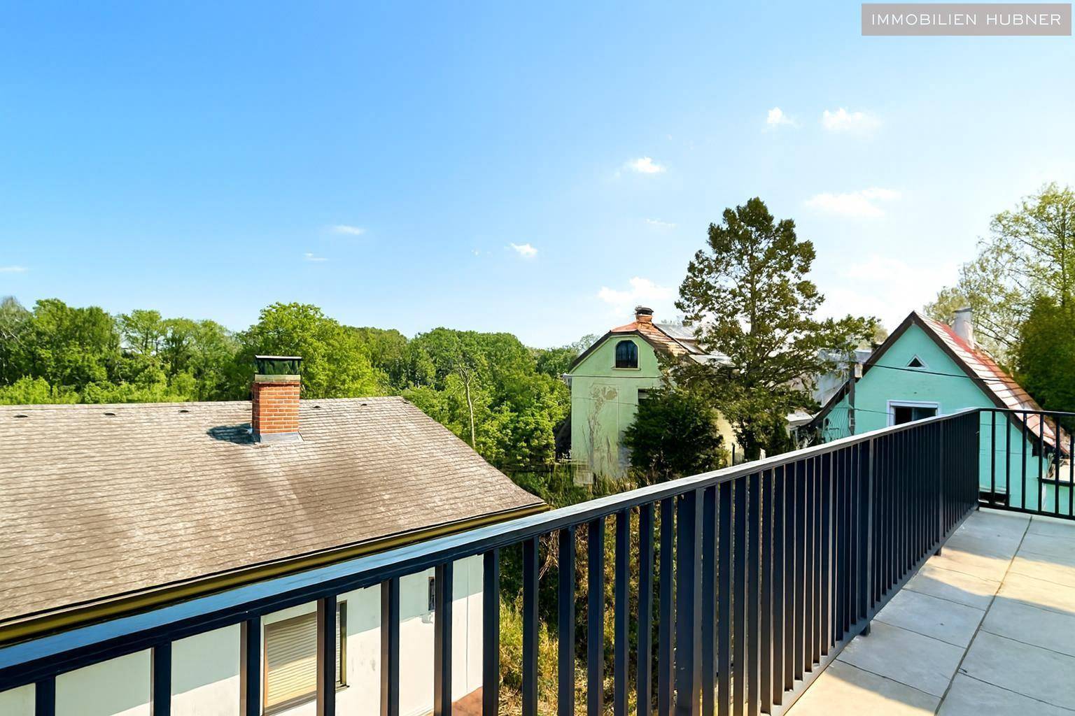Weitläufige Terrasse mit weitem Blick über die grüne Landschaft und umliegende Häuser, sehr idyllisch.