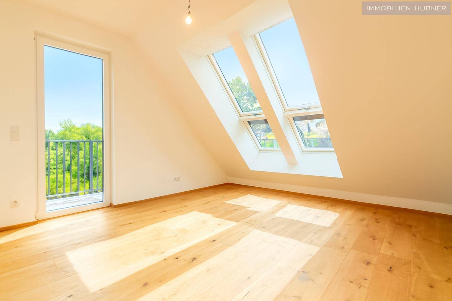 Heller Wohnraum mit Holzboden, großen Dachfenstern und Balkonzugang, bietet viel Tageslicht.