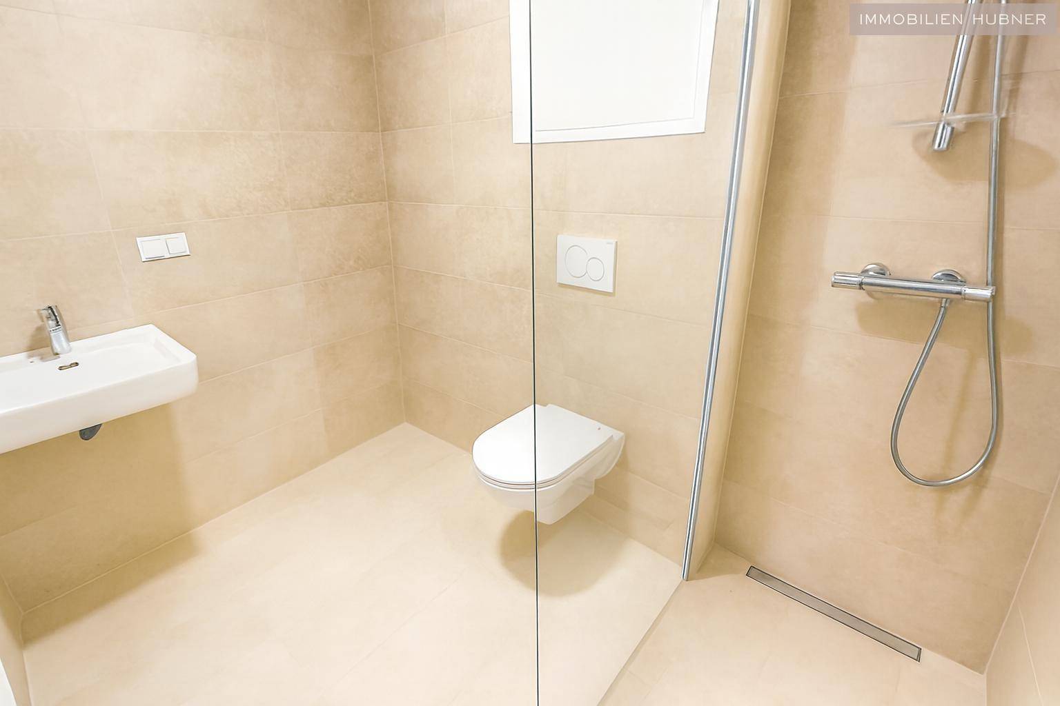 Modernes Badezimmer mit beigefarbenen Fliesen, wandhängendem WC und ebenerdiger Dusche, sehr gepflegt.