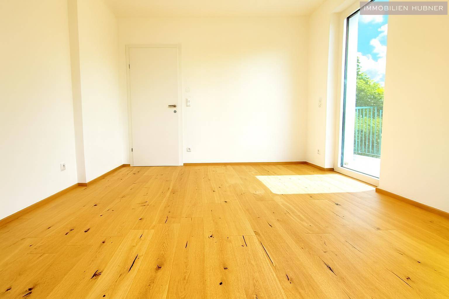 Geräumiger, heller Raum mit Holzboden und Zugang zu einem kleinen Balkon, vielseitig nutzbar.