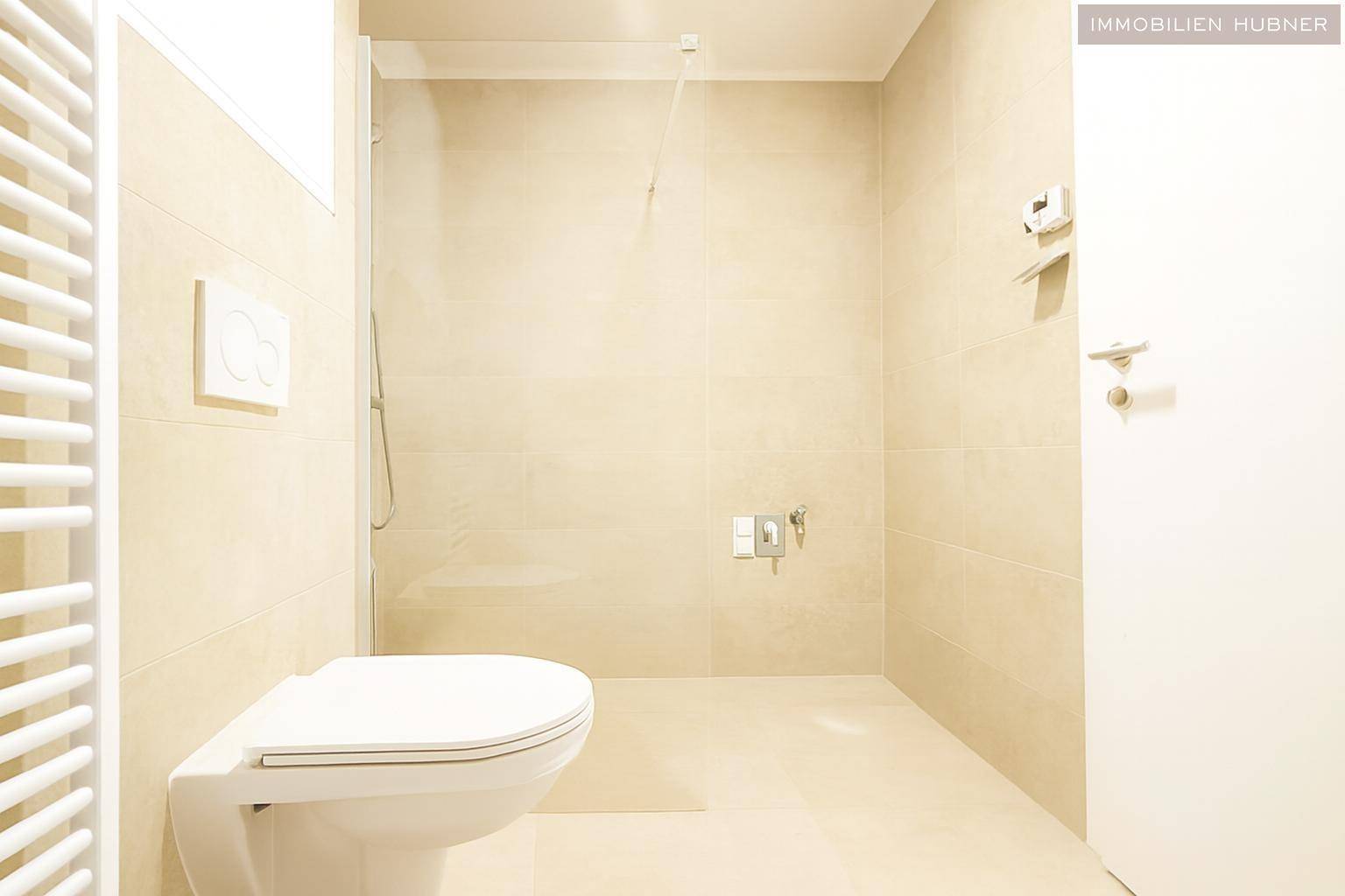 Helles Badezimmer mit beigefarbenen Fliesen, Dusche und Wand-WC.