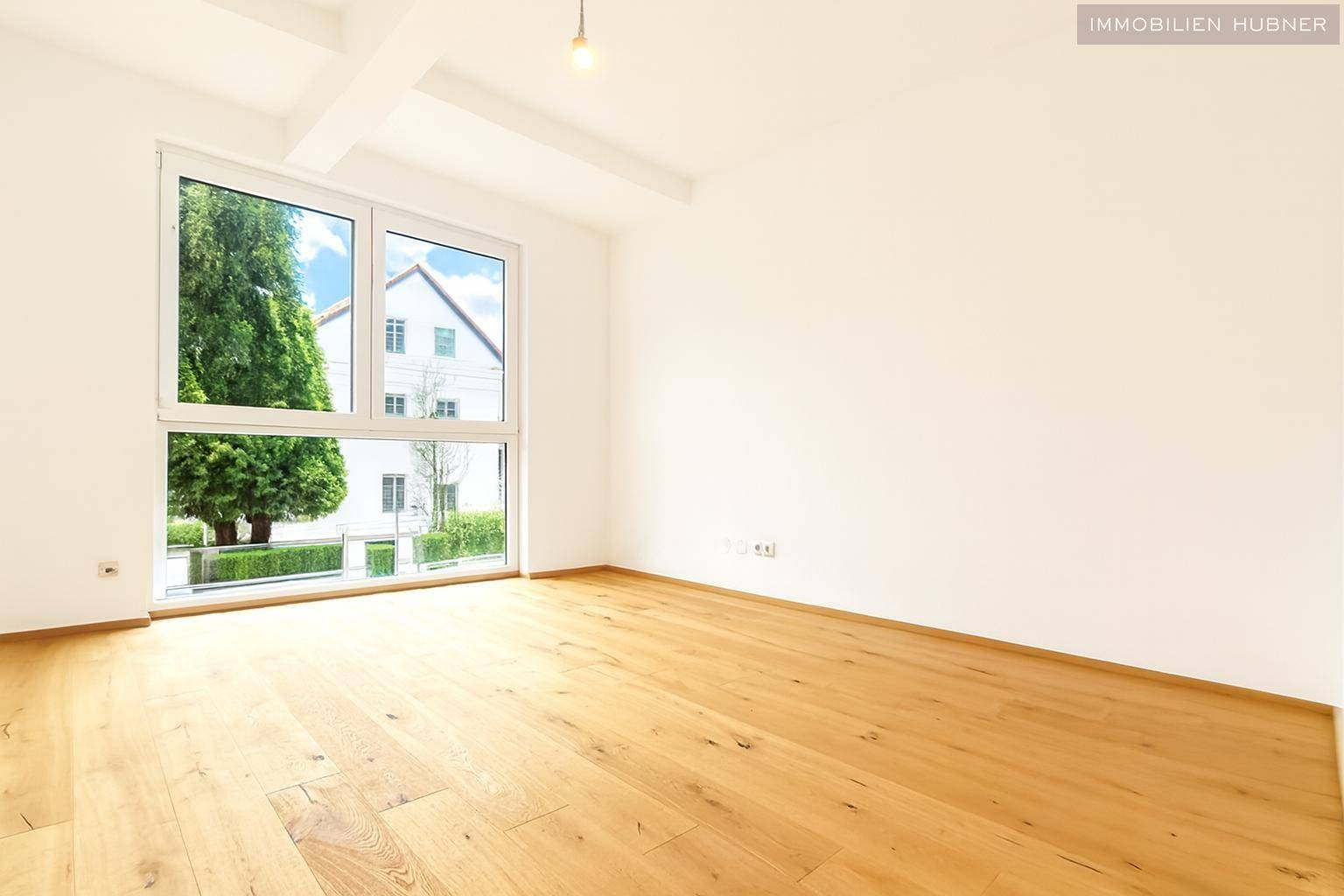 Geräumiges Zimmer mit großen Fenstern, Parkettboden und Blick ins Grüne.