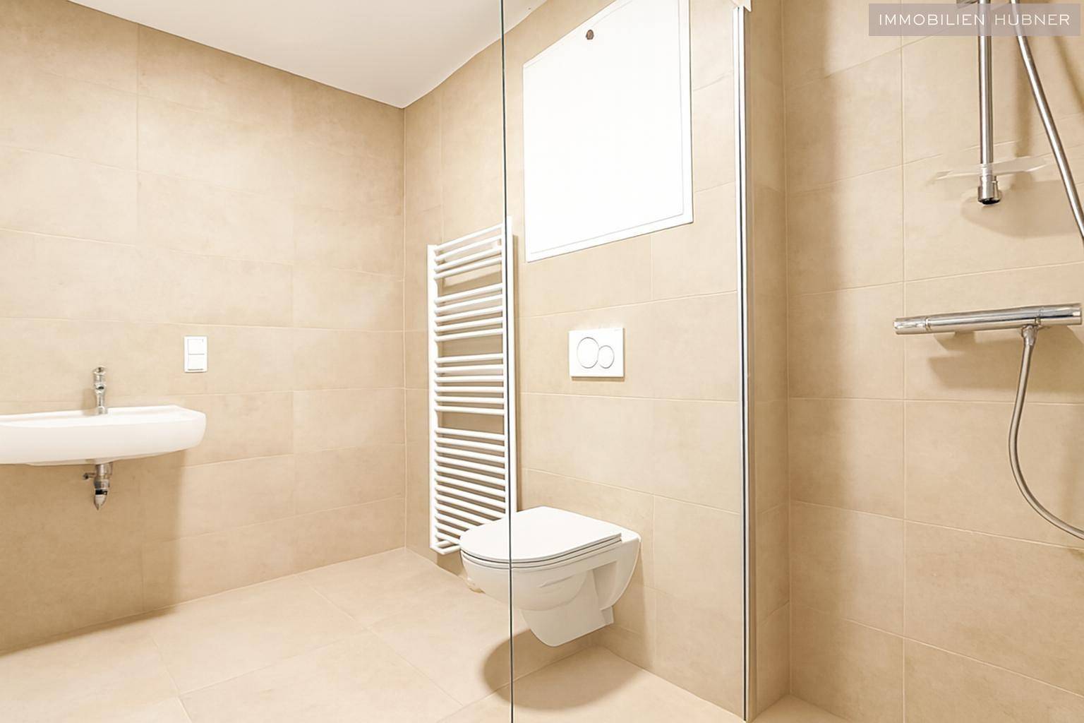 Modernes Badezimmer mit beigefarbenen Fliesen, Dusche und Wand-WC.