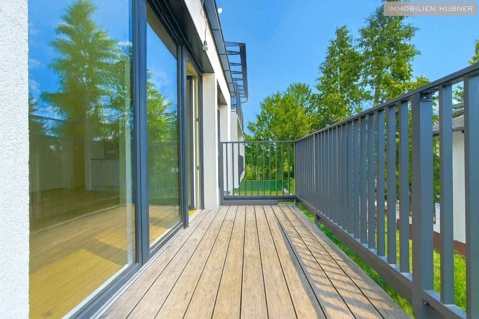 Moderner Balkon mit Holzboden und Blick auf Bäume und den Himmel.