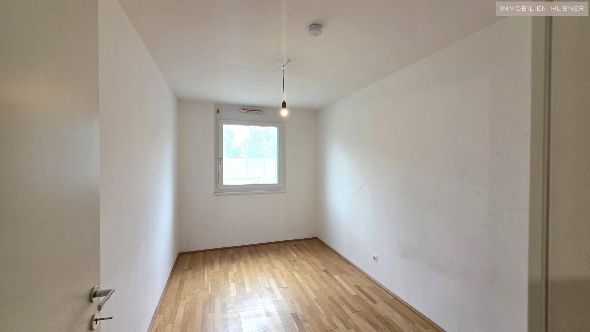Schlafzimmer mit Parkettboden, weiß gestrichenen Wänden und einem Fenster.