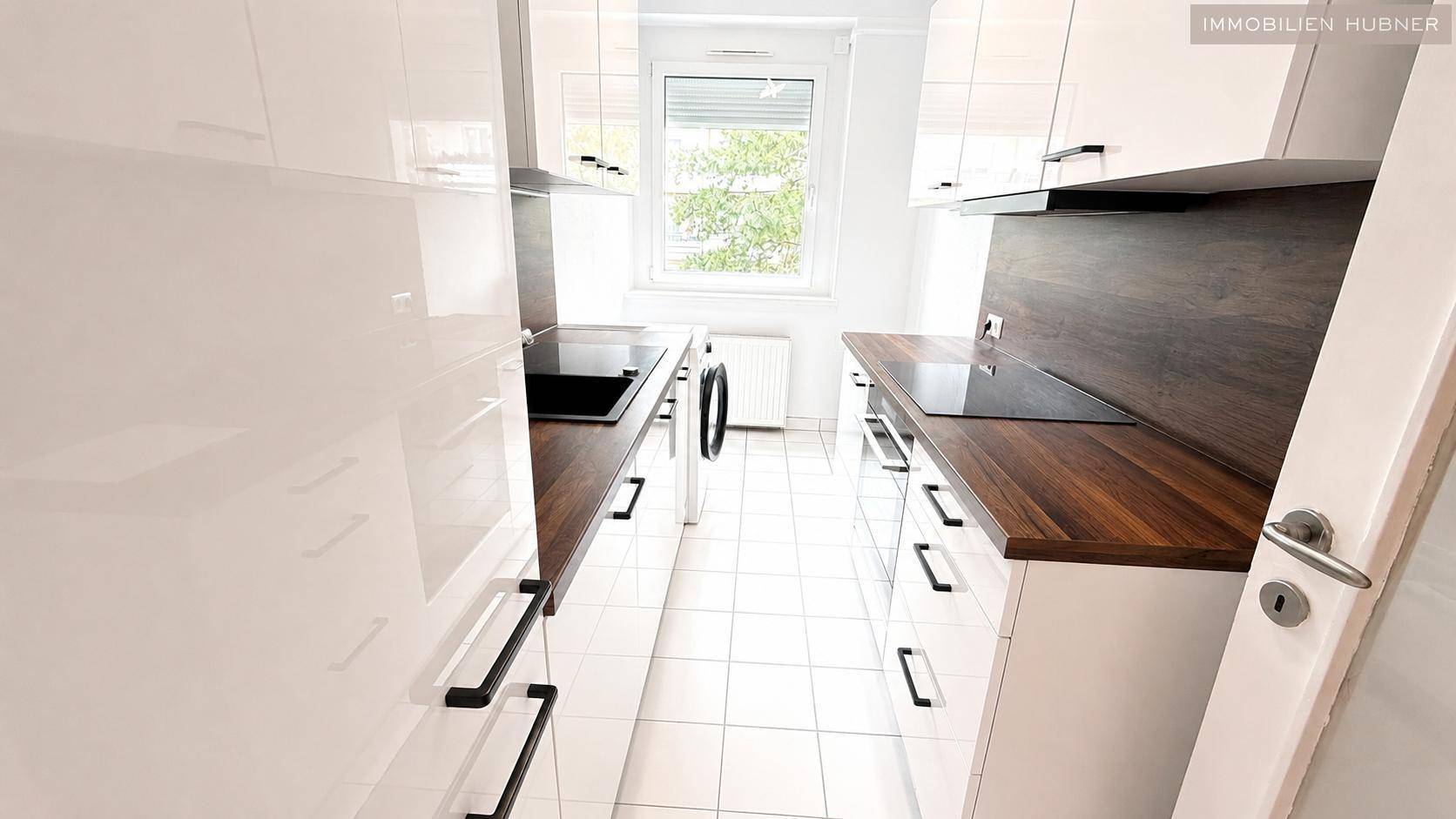 Moderne, helle Küche mit weißen Hochglanzfronten, Holz-Arbeitsplatten und Fensterblick ins Grüne.