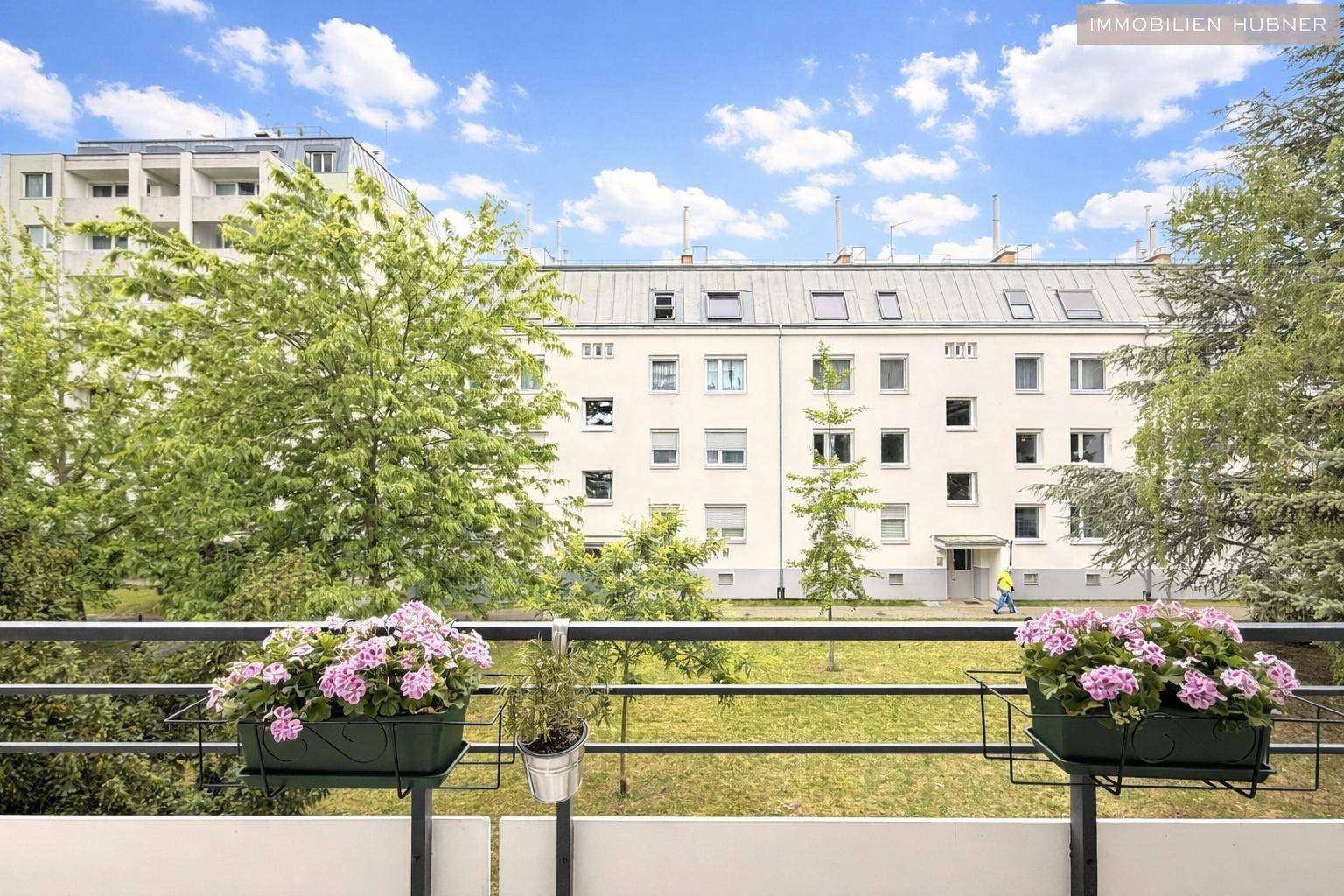 Blick vom Balkon auf die grüne Umgebung mit Bäumen und angrenzenden Wohngebäuden.