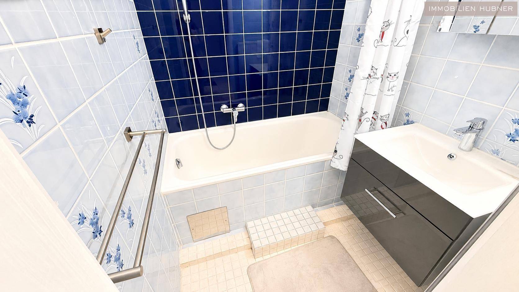 Badezimmer mit Badewanne, Waschbecken und blauen Fliesen, funktional und hell.