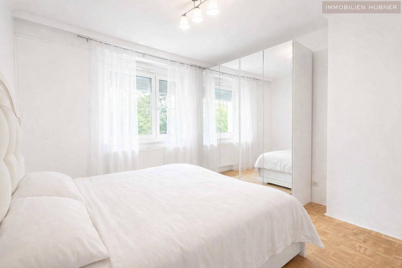 Helles Schlafzimmer mit großem Doppelbett, Spiegelschrank und Parkettboden, bietet viel Tageslicht.