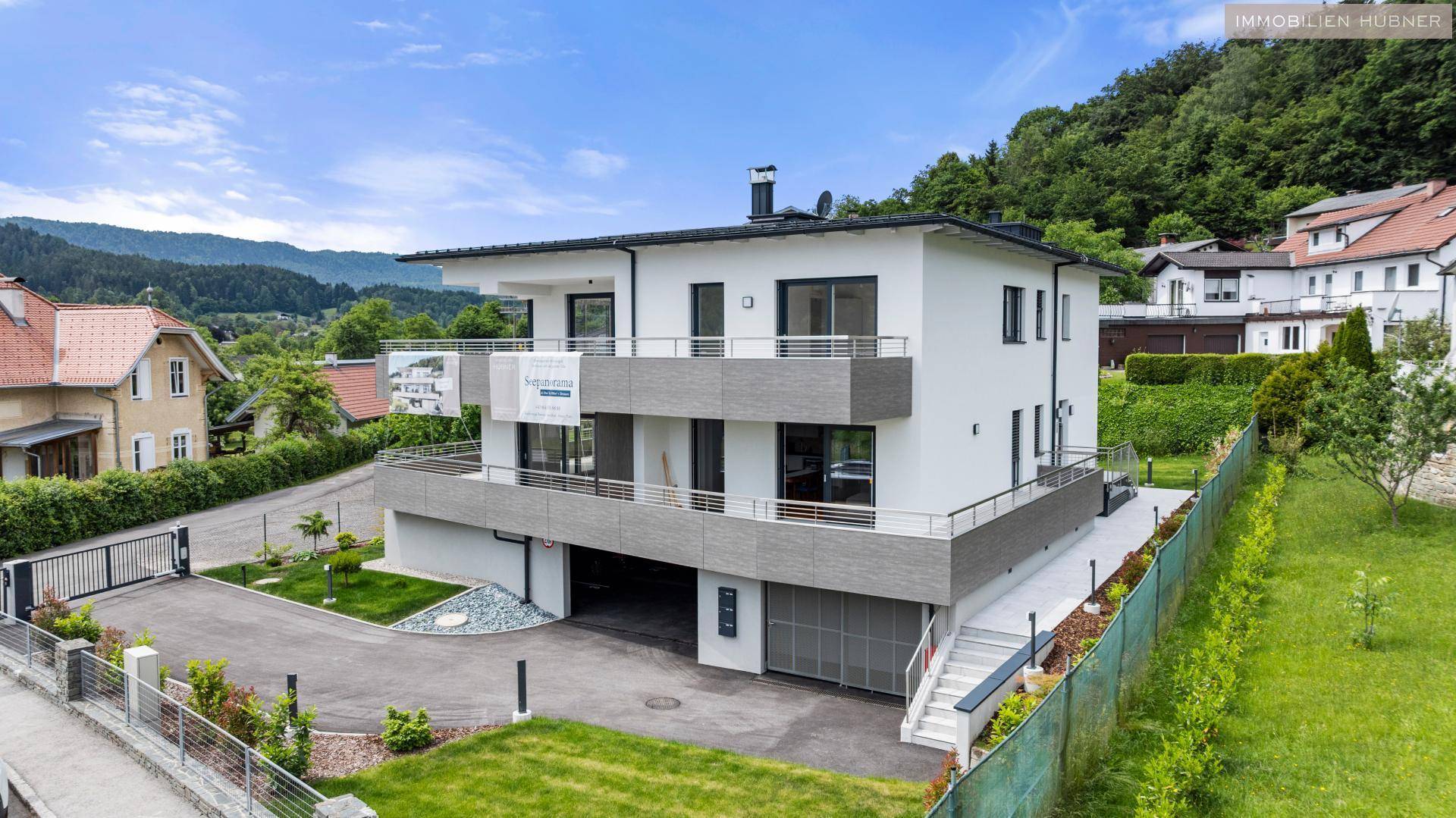 Modernes Mehrfamilienhaus mit mehreren Balkonen und Tiefgaragenzufahrt in grüner Umgebung.