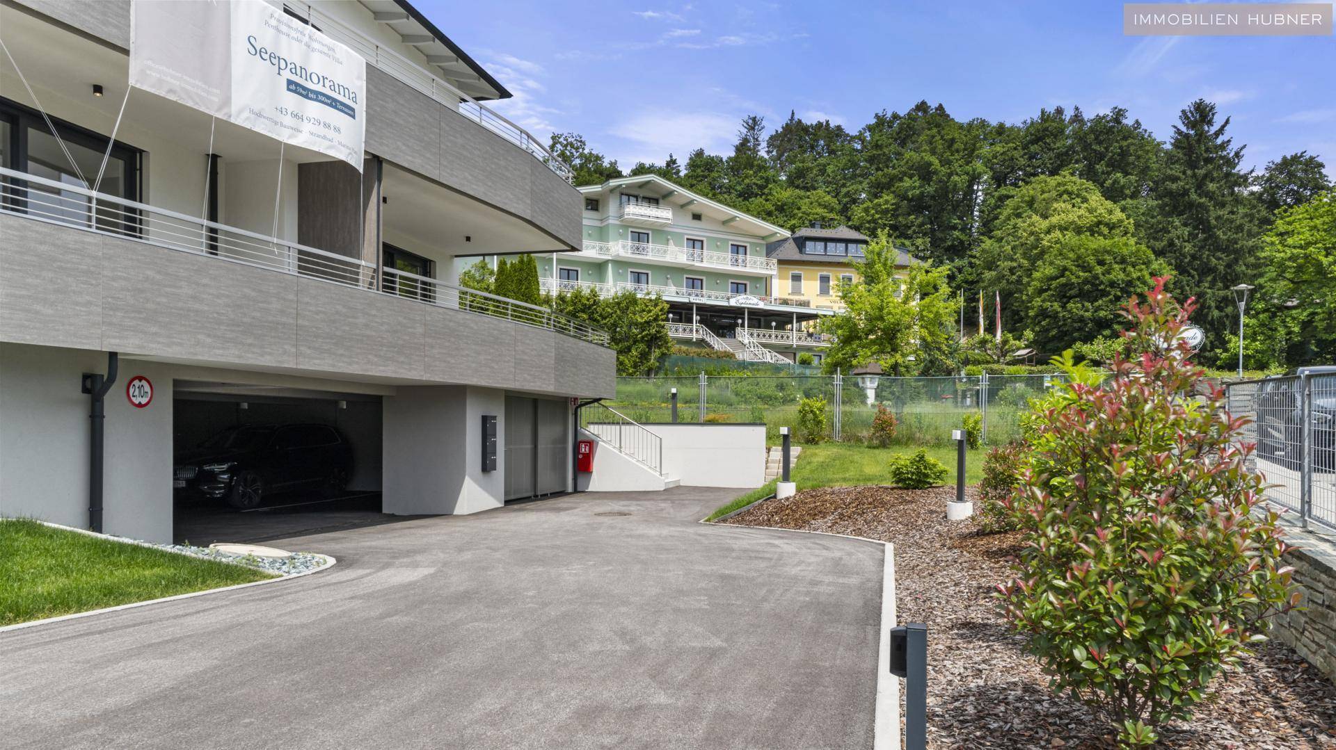 Zufahrt zu einem modernen Gebäude mit Tiefgarage und gepflegter Bepflanzung am Hang.