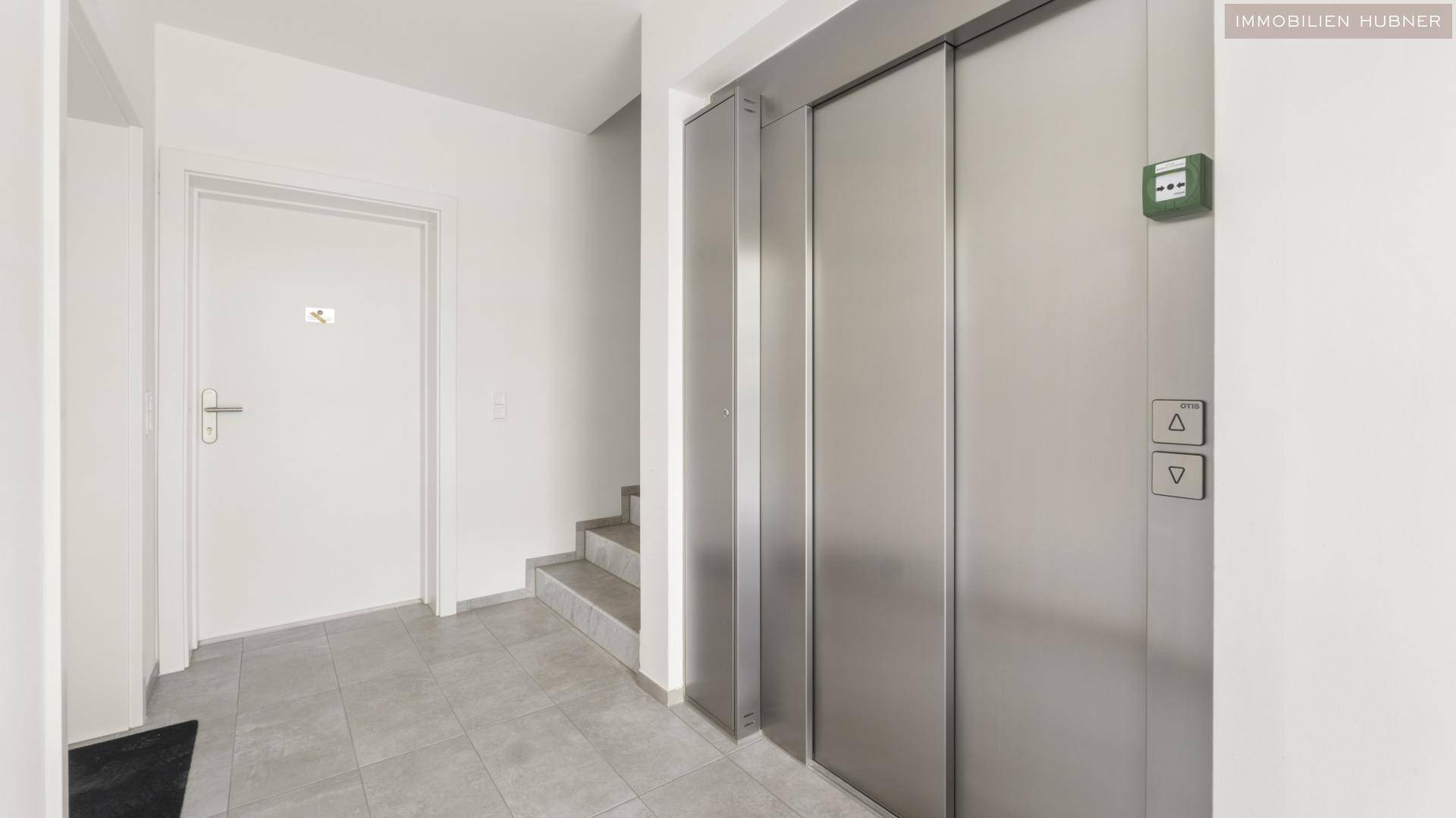 Moderner Eingangsbereich mit Fliesenboden, Aufzug und Treppenhaus in einem Mehrfamilienhaus.