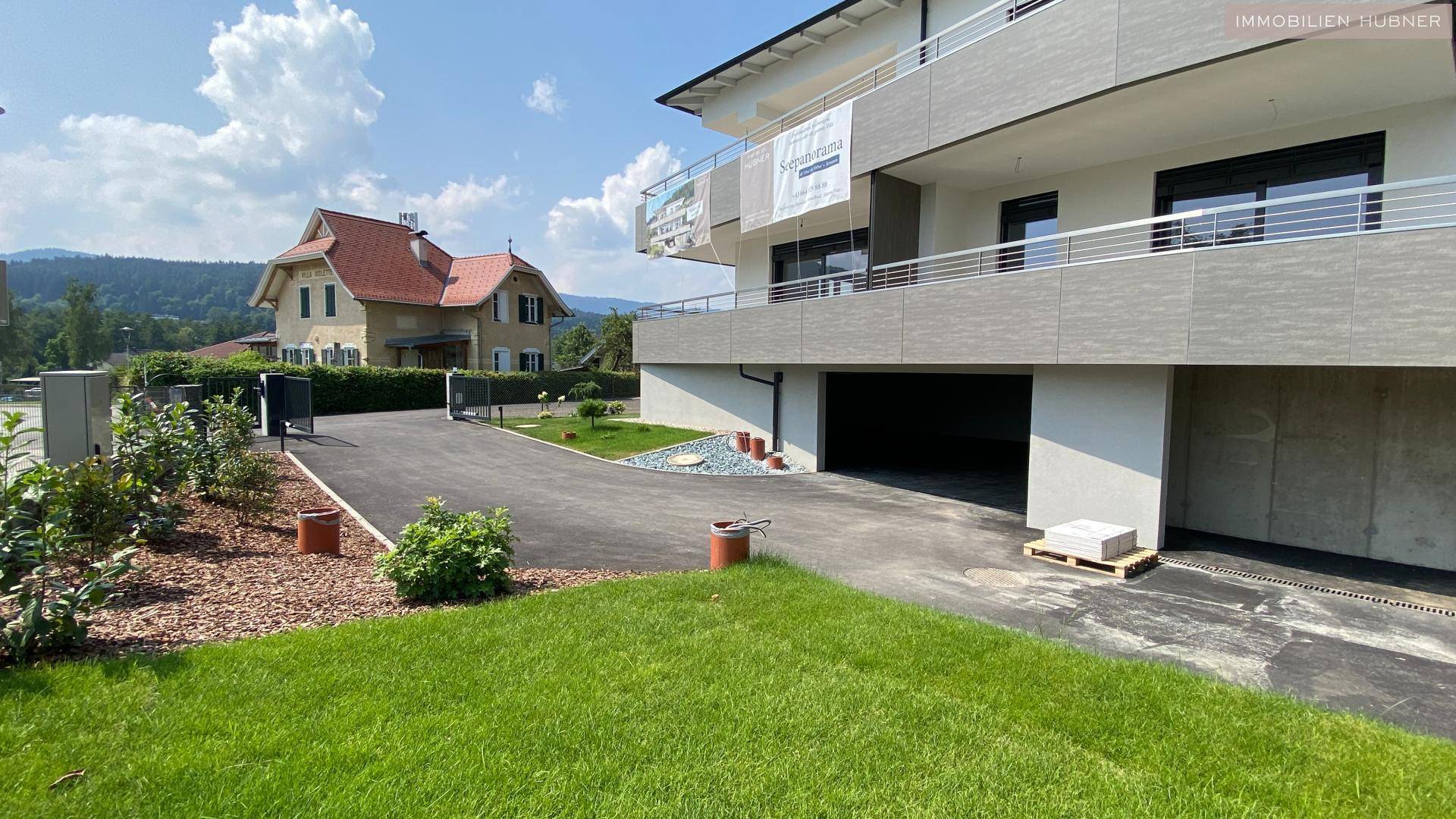 Seitenansicht eines modernen Gebäudes mit Tiefgaragenzufahrt und gepflegter Grünfläche.