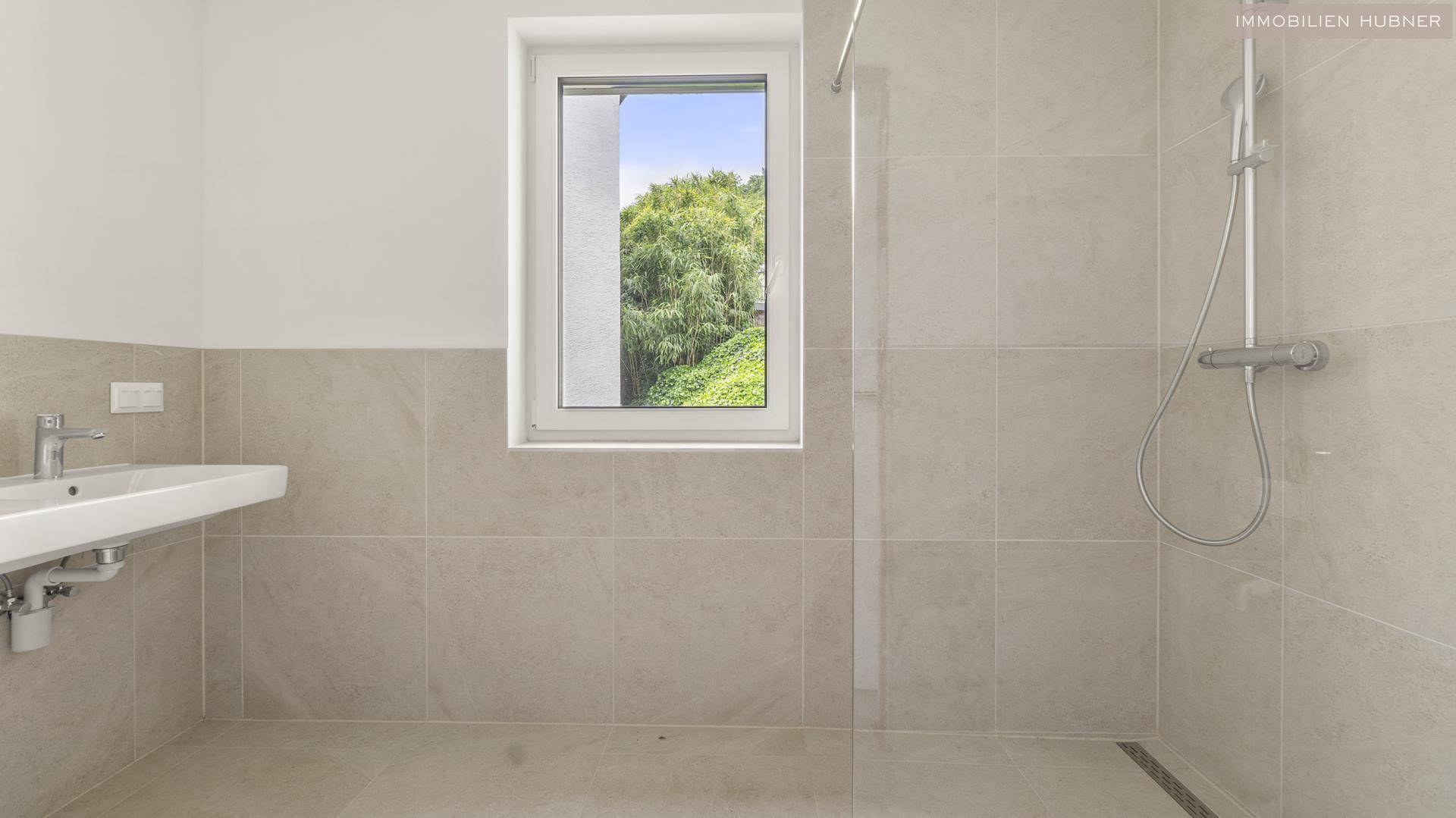 Modernes Badezimmer mit begehbarer Dusche, Waschbecken und Fenster mit Blick ins Grüne.
