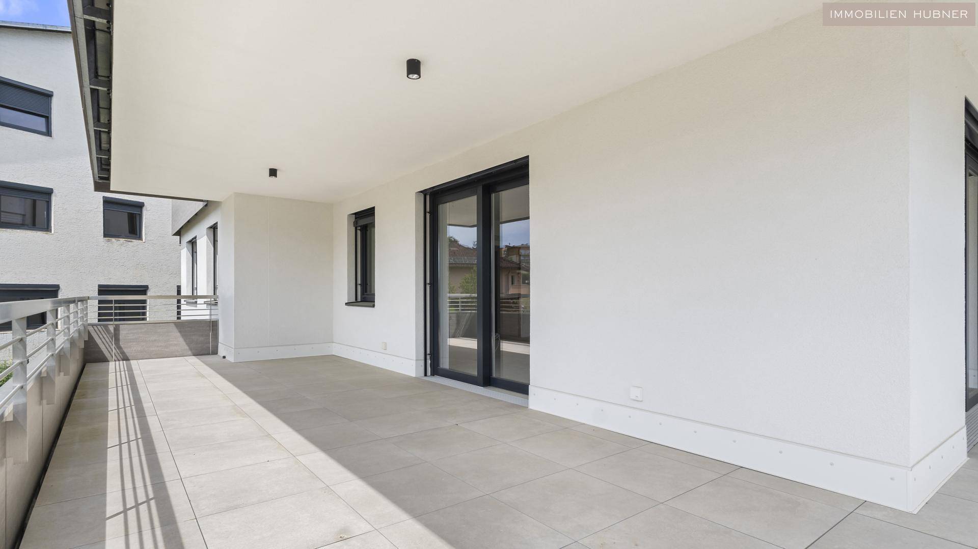 Großer, leerer Balkon mit Fliesenboden und Zugang zu Innenräumen durch Schiebetüren.