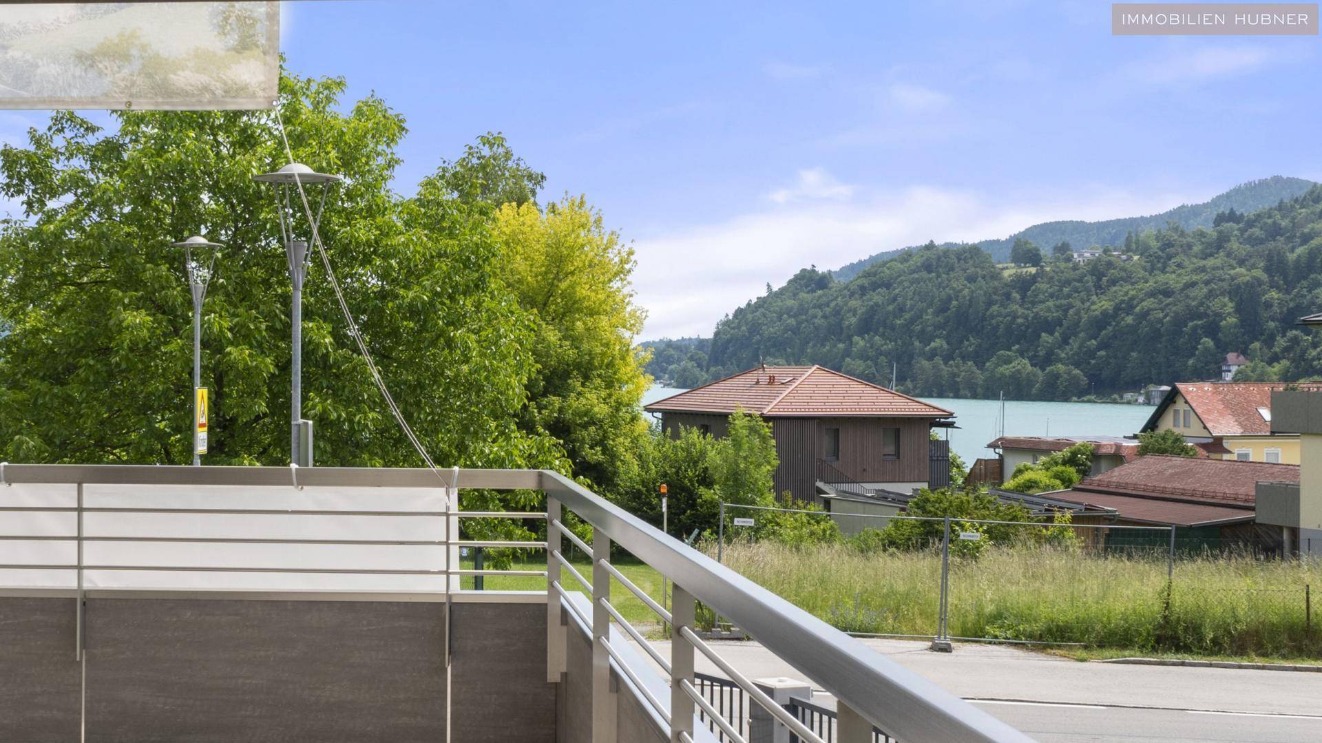 Malerischer Blick von einem Balkon auf den See, grüne Bäume und die umliegende Landschaft.