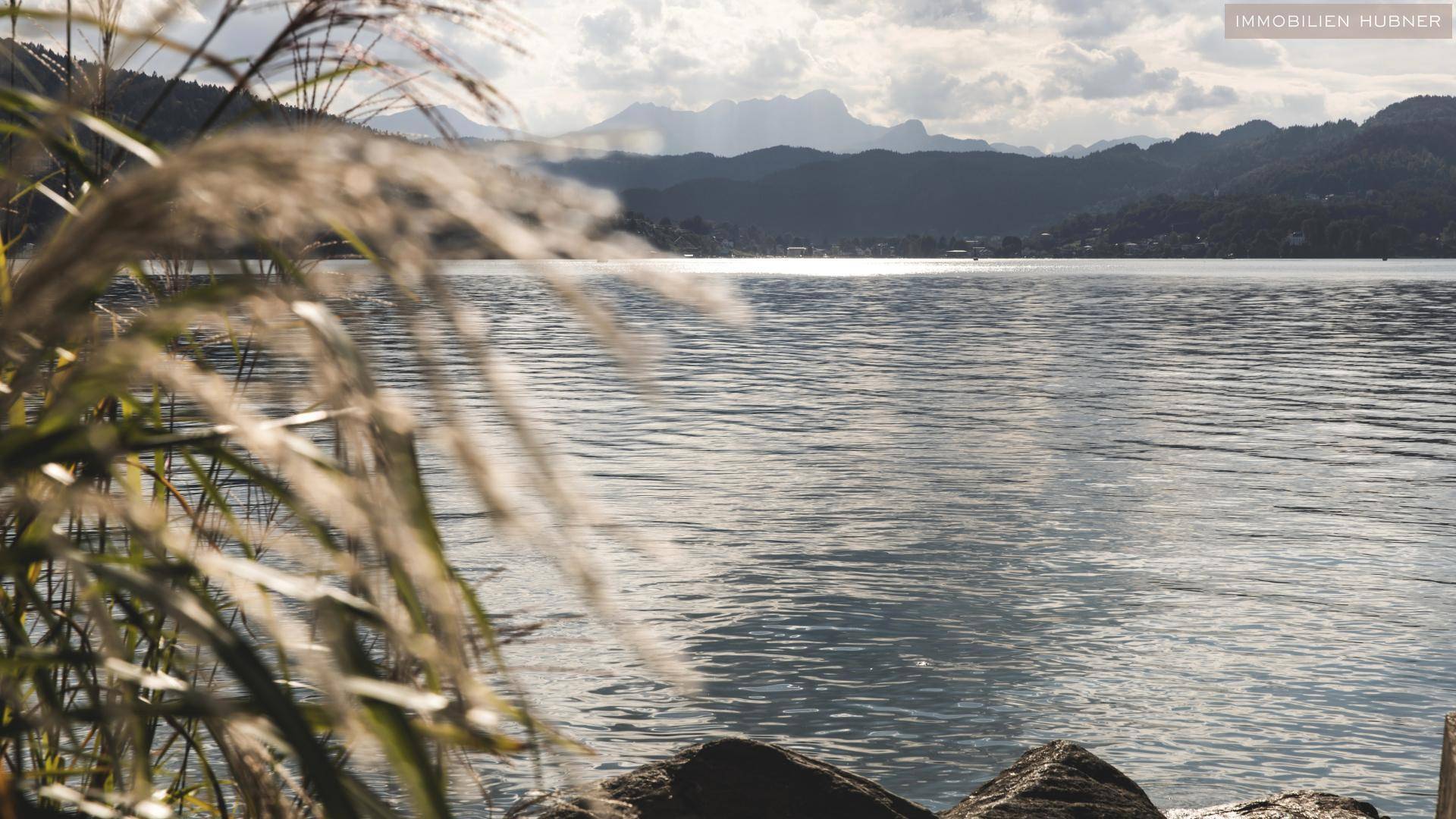 Malerischer Blick auf einen See mit Bergen im Hintergrund und Schilf im Vordergrund.