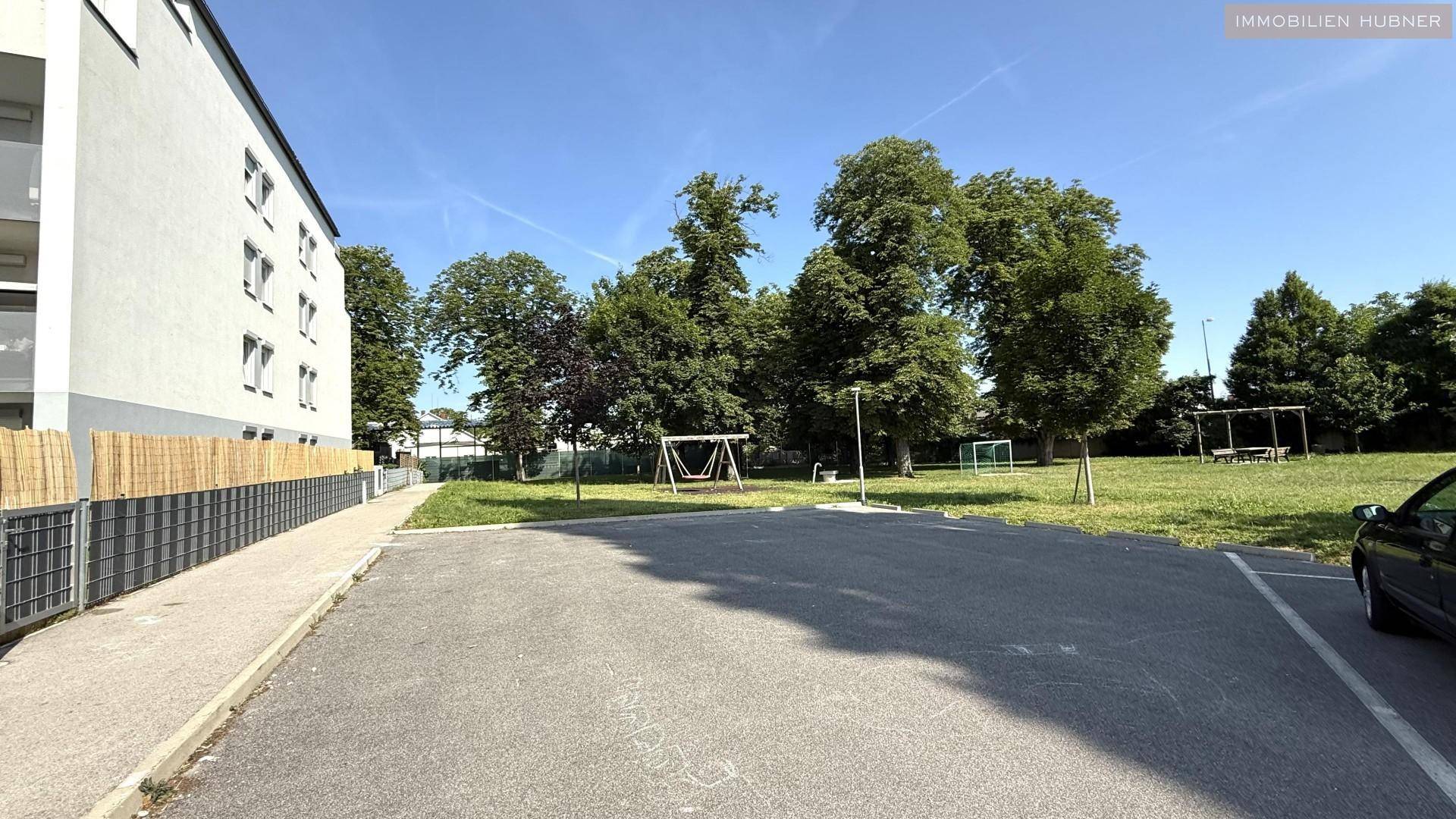 Parkplatzbereich neben dem Gebäude mit angrenzendem Spielplatz und Grünflächen.
