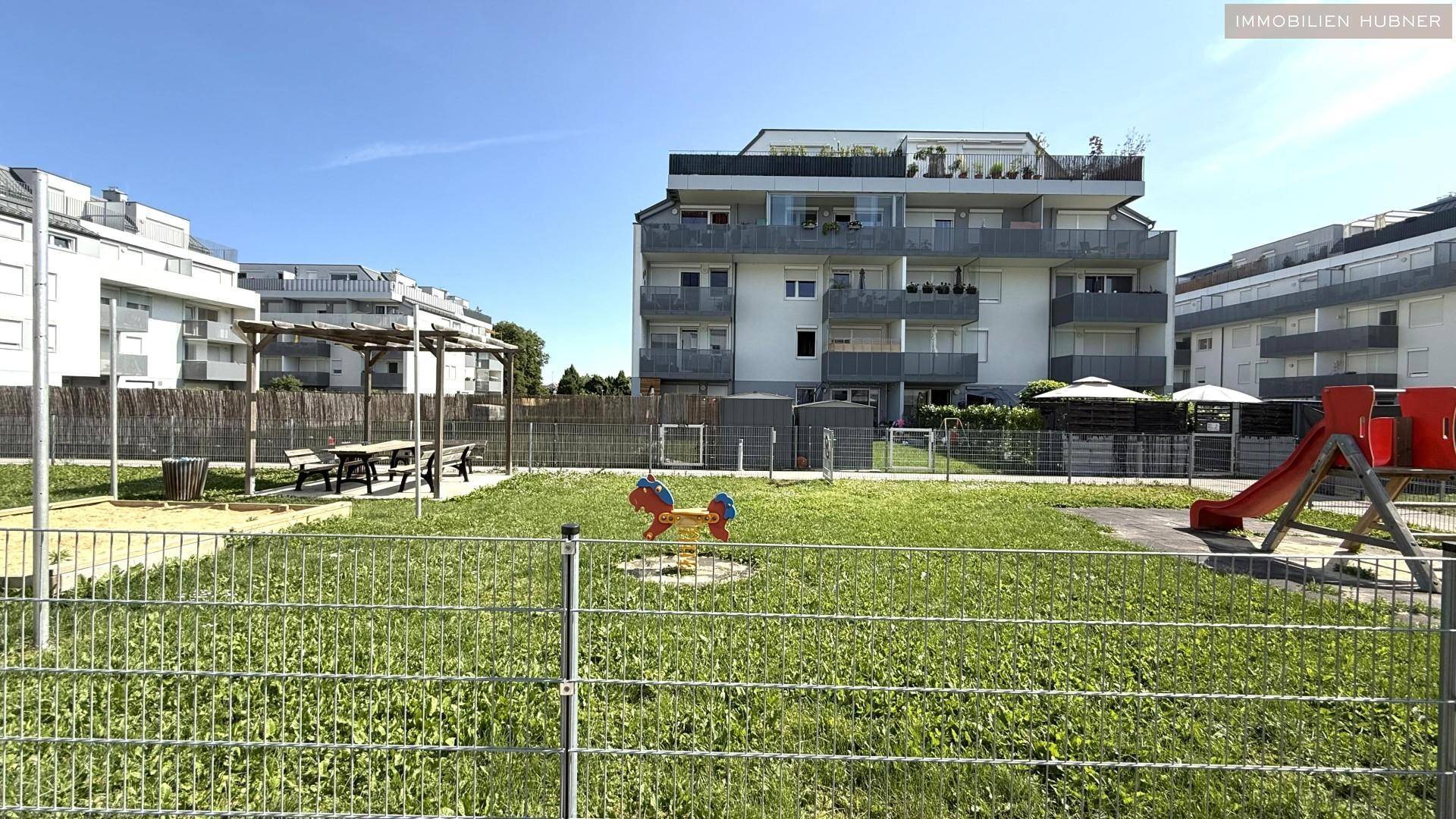 Kinderspielplatz mit Rutsche und Federwippe, umgeben von Grünflächen und Wohngebäuden.